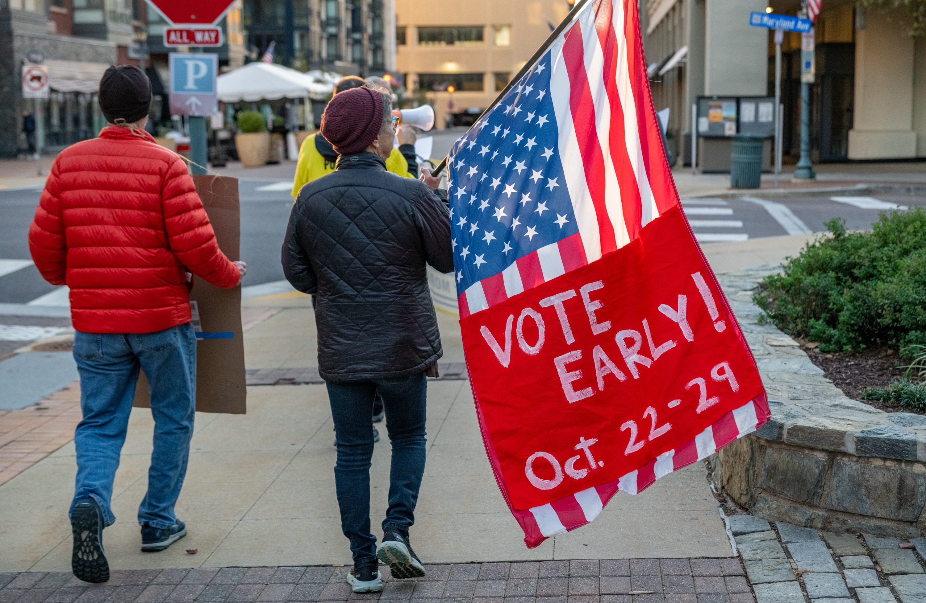 Susan Friend carries a flag as she marches to the early voting poll at the Montgomery County Executive Office Building in Rockville on the first day of early voting on Thursday.