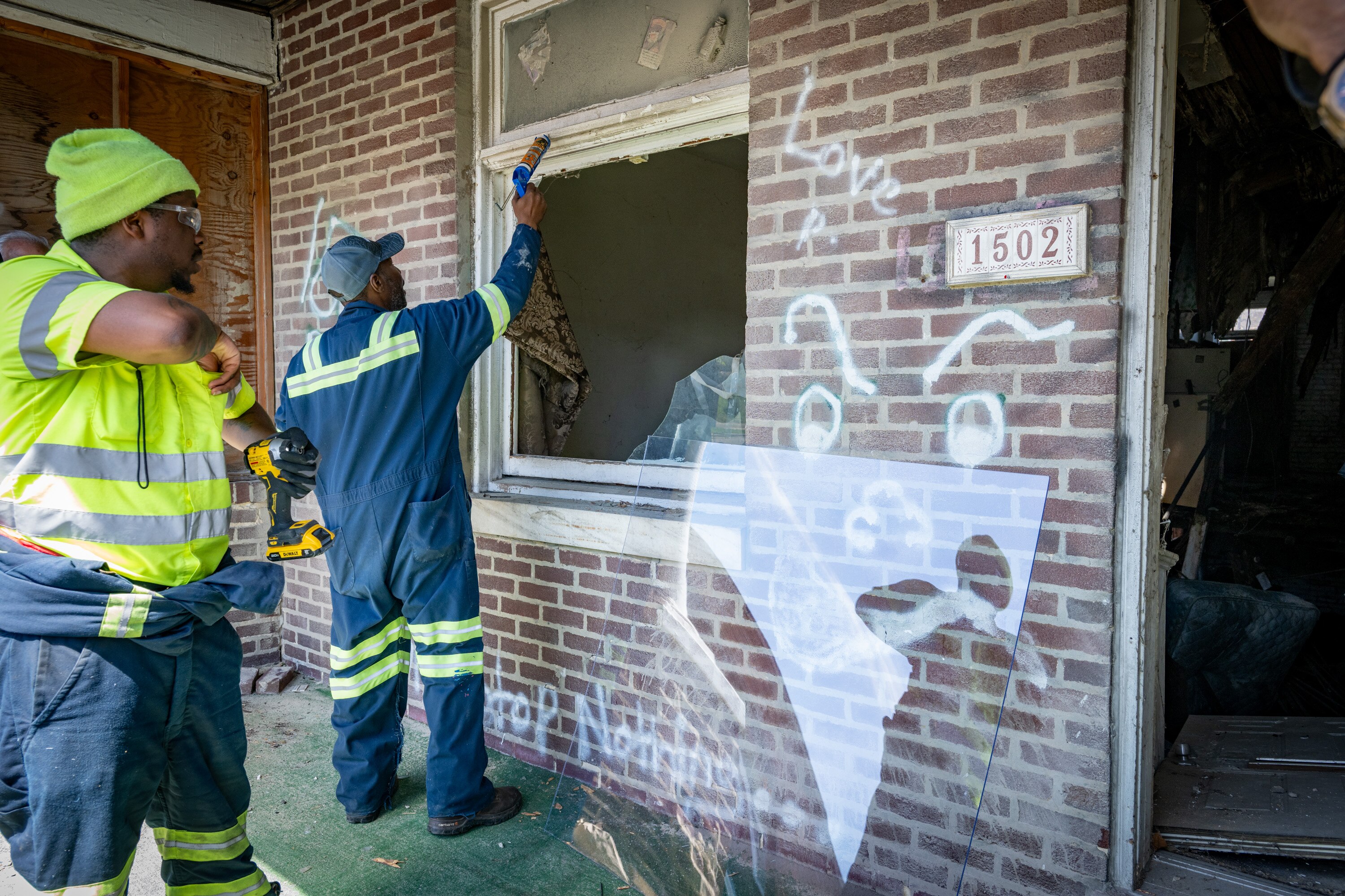 Baltimore Department of Public Works employees prepare to replace plywood with a polycarbonate sheet on a vacant home in the Coldstream Homestead Montebello community.