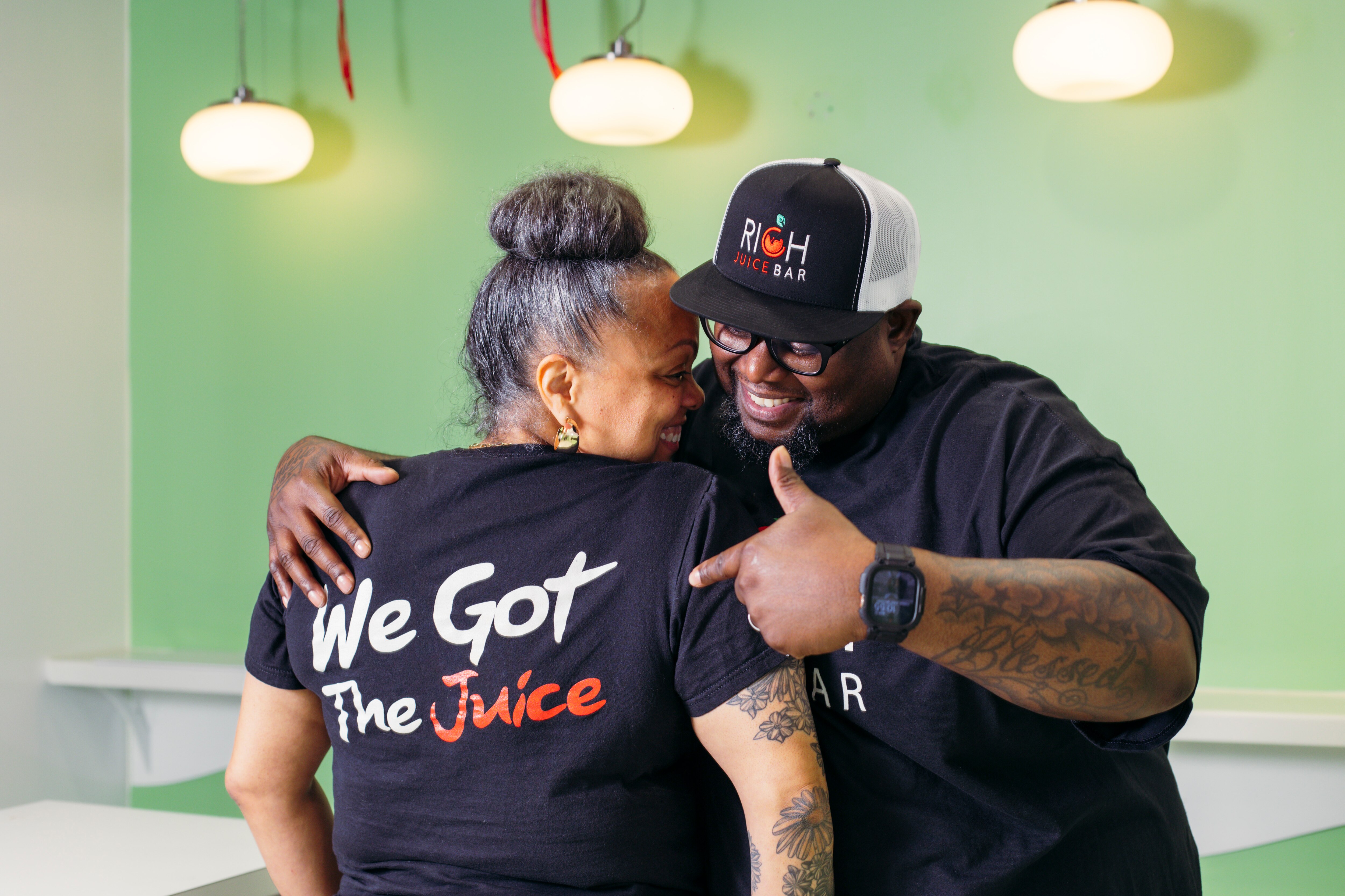 Dani and Michael Battle, owners of RICH Juice Bar, show off their company shirts inside their new location in the Light Street Pavilion, on Wednesday, April 17, 2024.