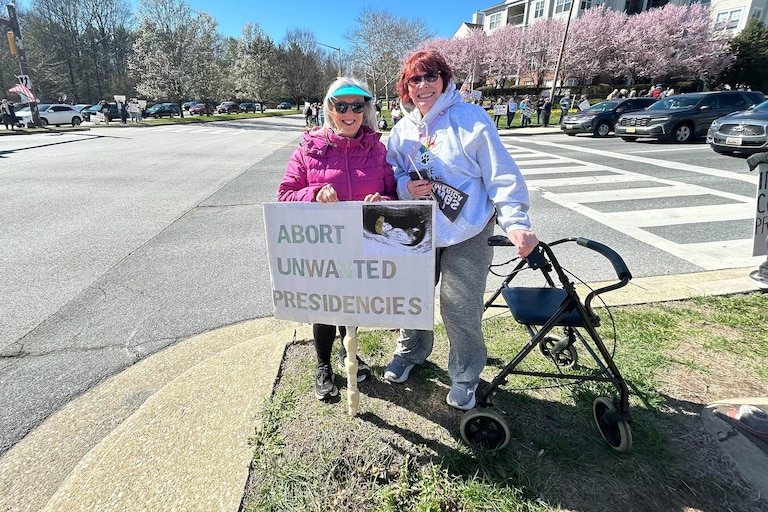 SATURDAY, MARCH 28, 2026 - Howard County residents and friends Karen Joy and Linda Bossard in the neutral ground at the intersection of Broken Land and Little Patuxent Parkways during the No Kings protest in Columbia.