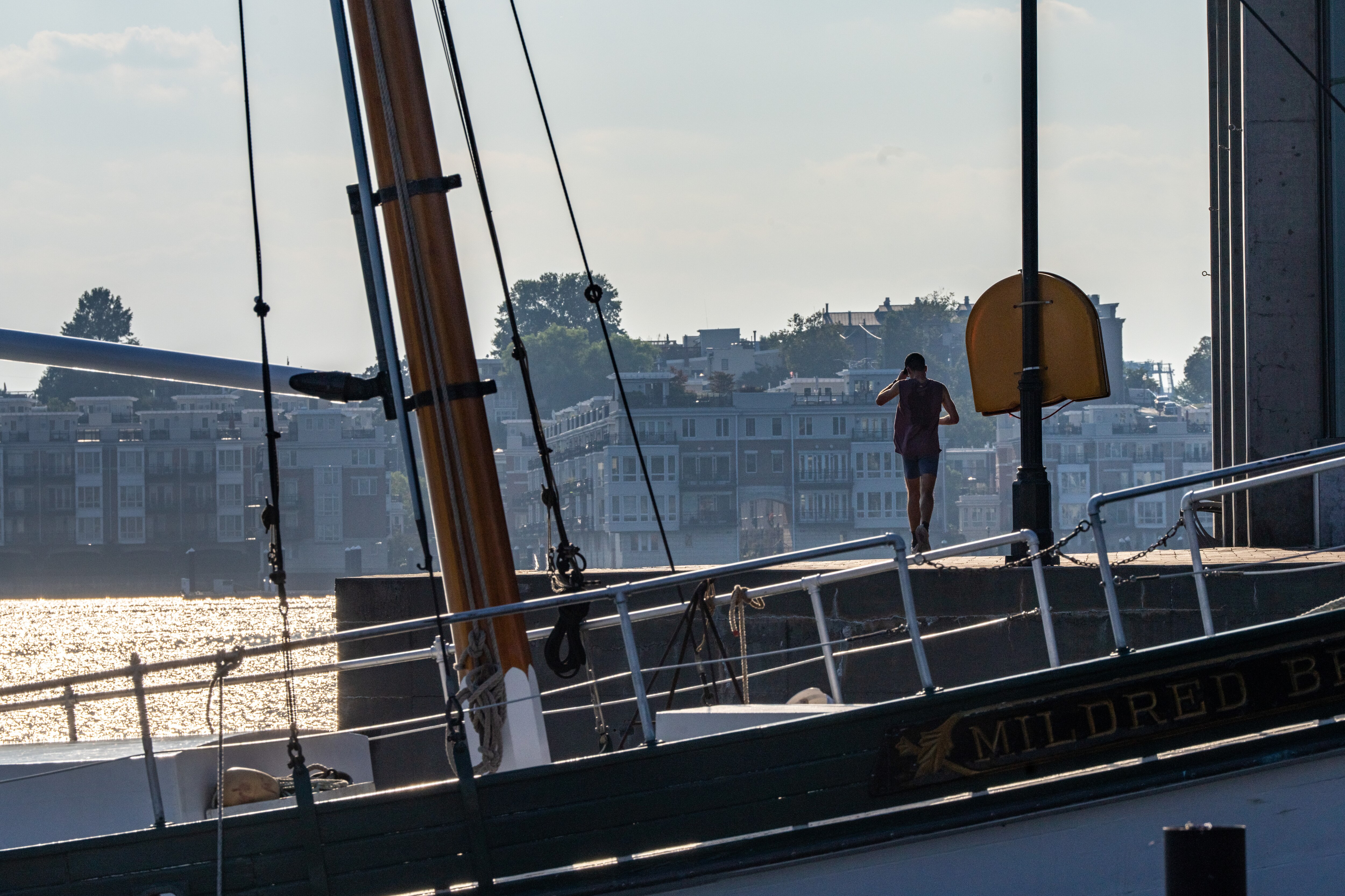 A man in silhouette adjusts his hat while running away from the camera. The Mildred Belle buyboat in the foreground frames the runner.