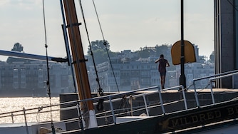 A man in silhouette adjusts his hat while running away from the camera. The Mildred Belle buyboat in the foreground frames the runner.