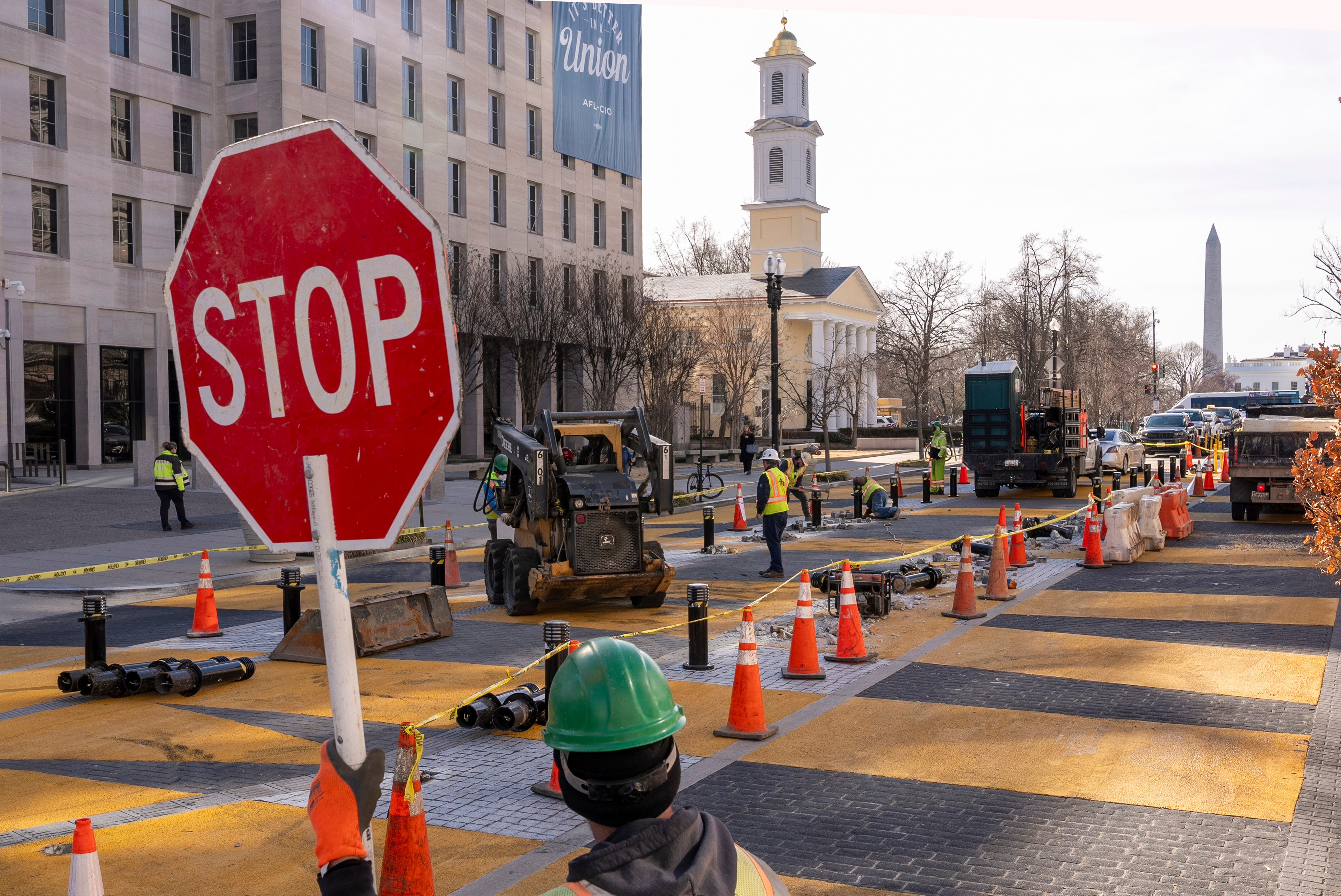 A red stop sign stands in the foreground, in front of demolition work removing "BLACK LIVES MATTER" mural from the streets of Washington, D.C. Several pieces of construction equipment can be seen, with St. John's Episcopal Church, the Washington Monument and The White House all in the background.