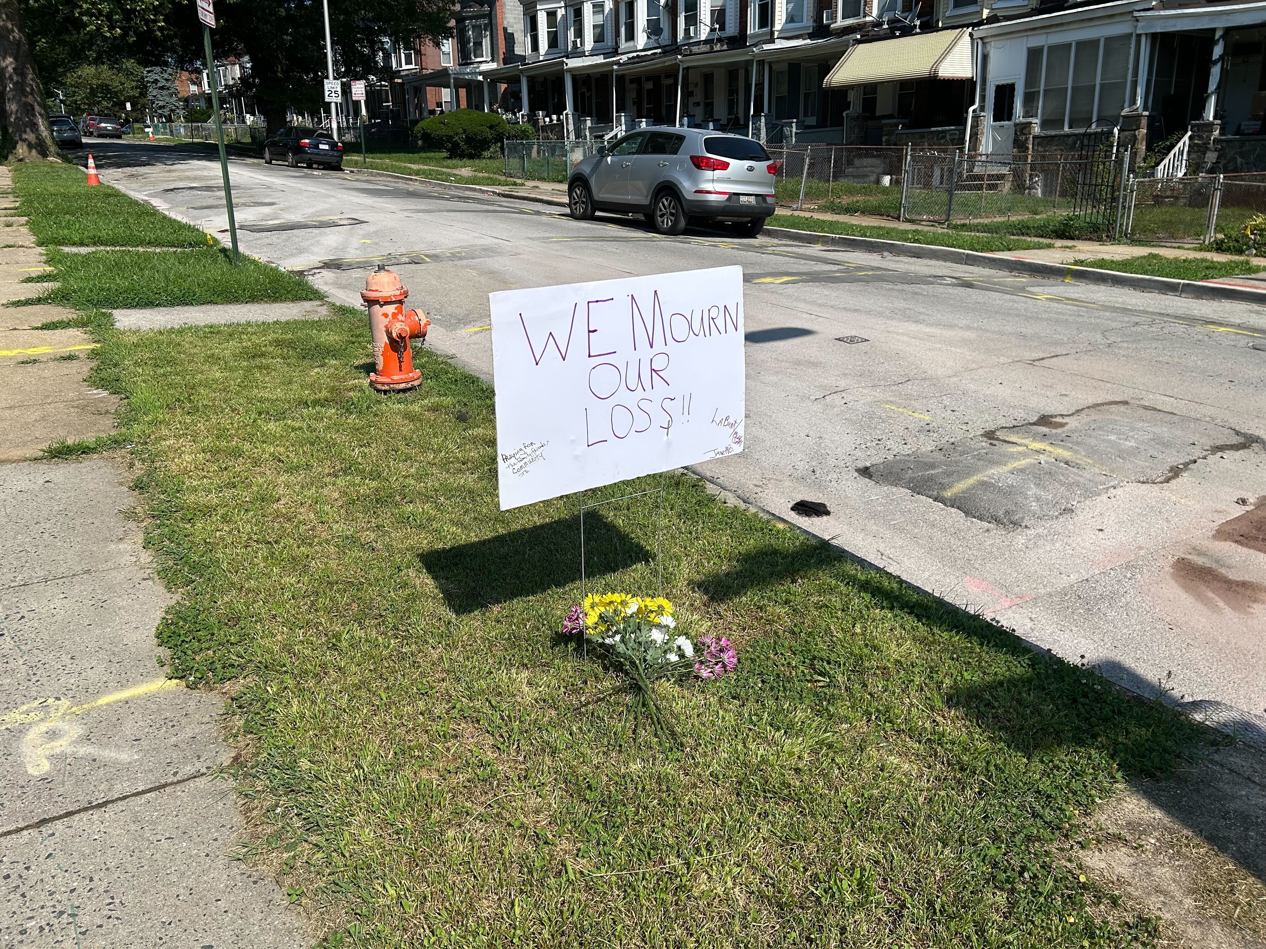 Janet Bailey, who runs a community fridge on Ashburton Street, placed flowers and a sign reading “We Mourn Our Loss” at Mosher and Ashburton on Thursday, June 26, 2025, urging others to add names and tributes for the 70-year-old woman fatally shot by police.