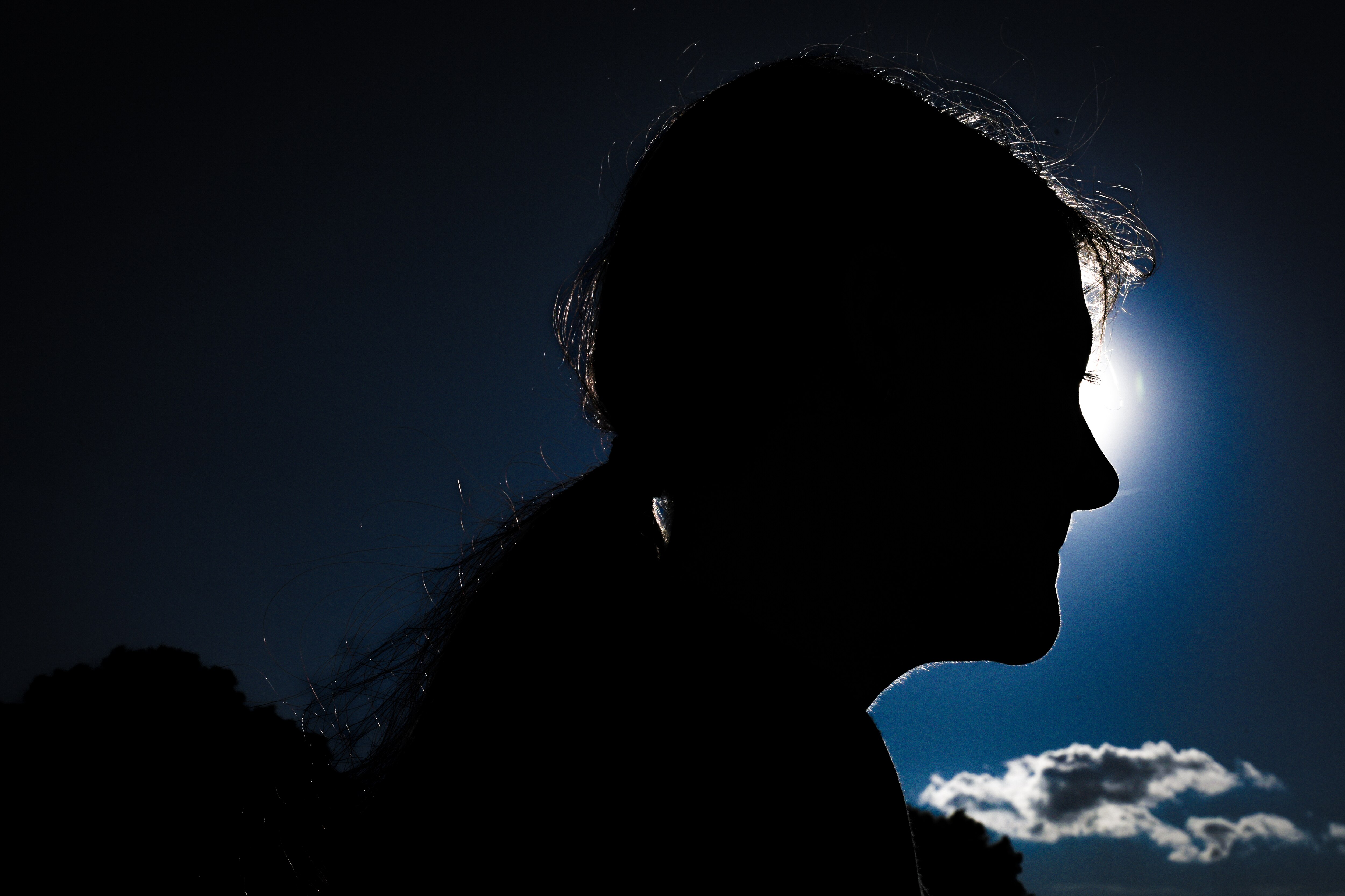 Silhouetted by the sun, a middle school girl who suffered a vicious attack by classmates stands for a photo outdoors.