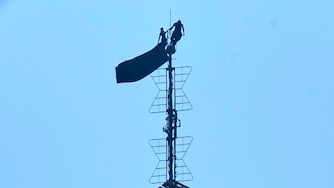 Two people stand on the tip of the antenna of the Empire State Building while holding a banner on Wednesday, July 1, 2026.