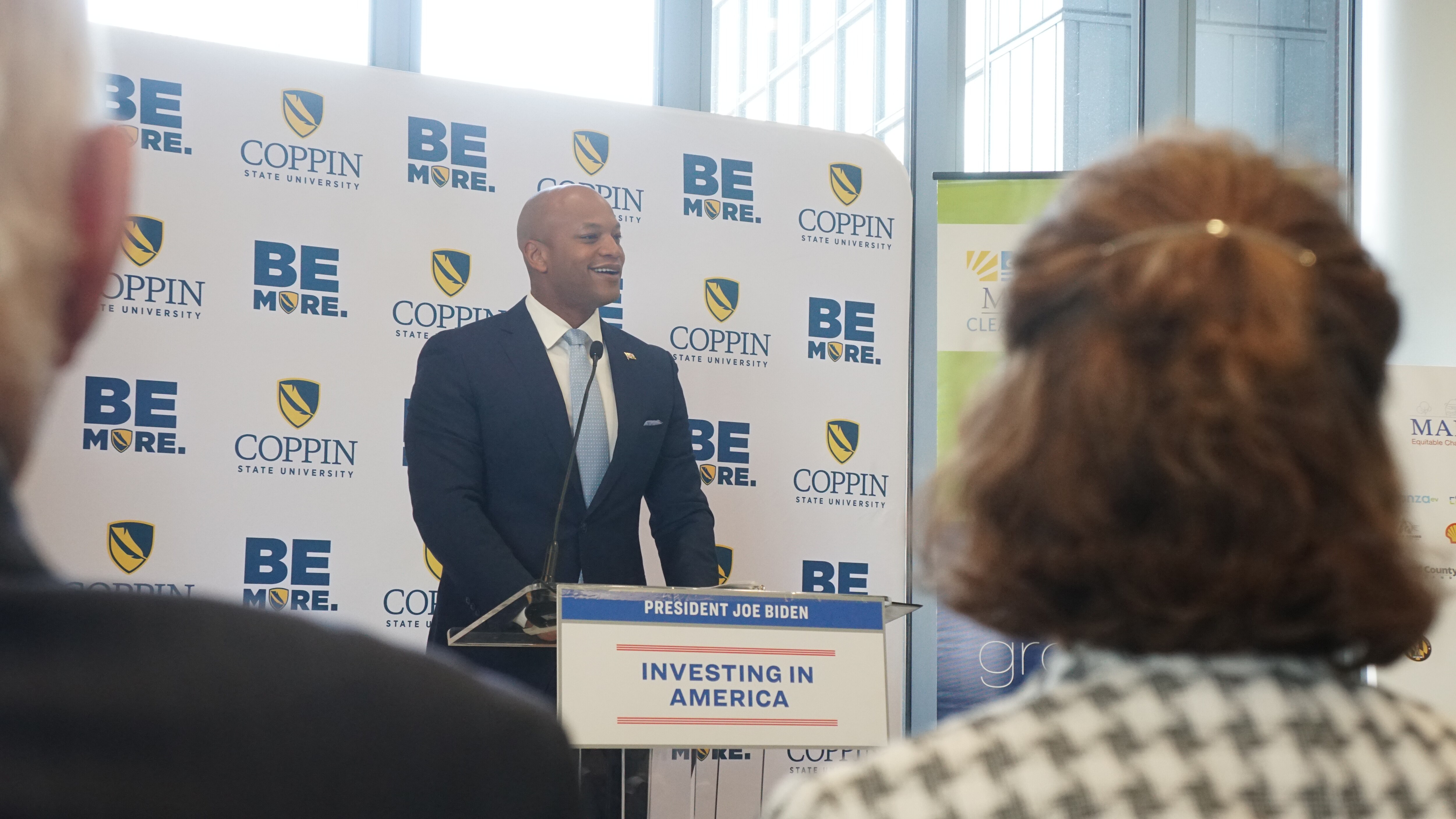 Maryland Gov. Wes Moore, dressed in a suit and light blue tie, smiles and delivers a speech in front of a white Coppin State University backdrop.