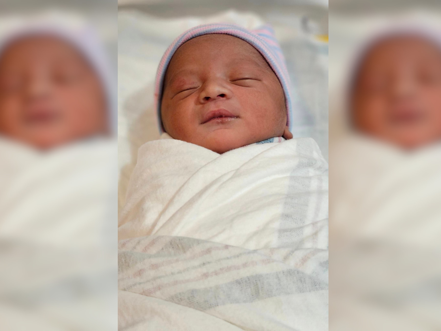 A newborn baby wrapped in a hospital swaddle with a pastel-striped hat on its head. The baby appears to be sleeping peacefully. The image is focused on the baby, with a softly blurred background to emphasize the subject.
