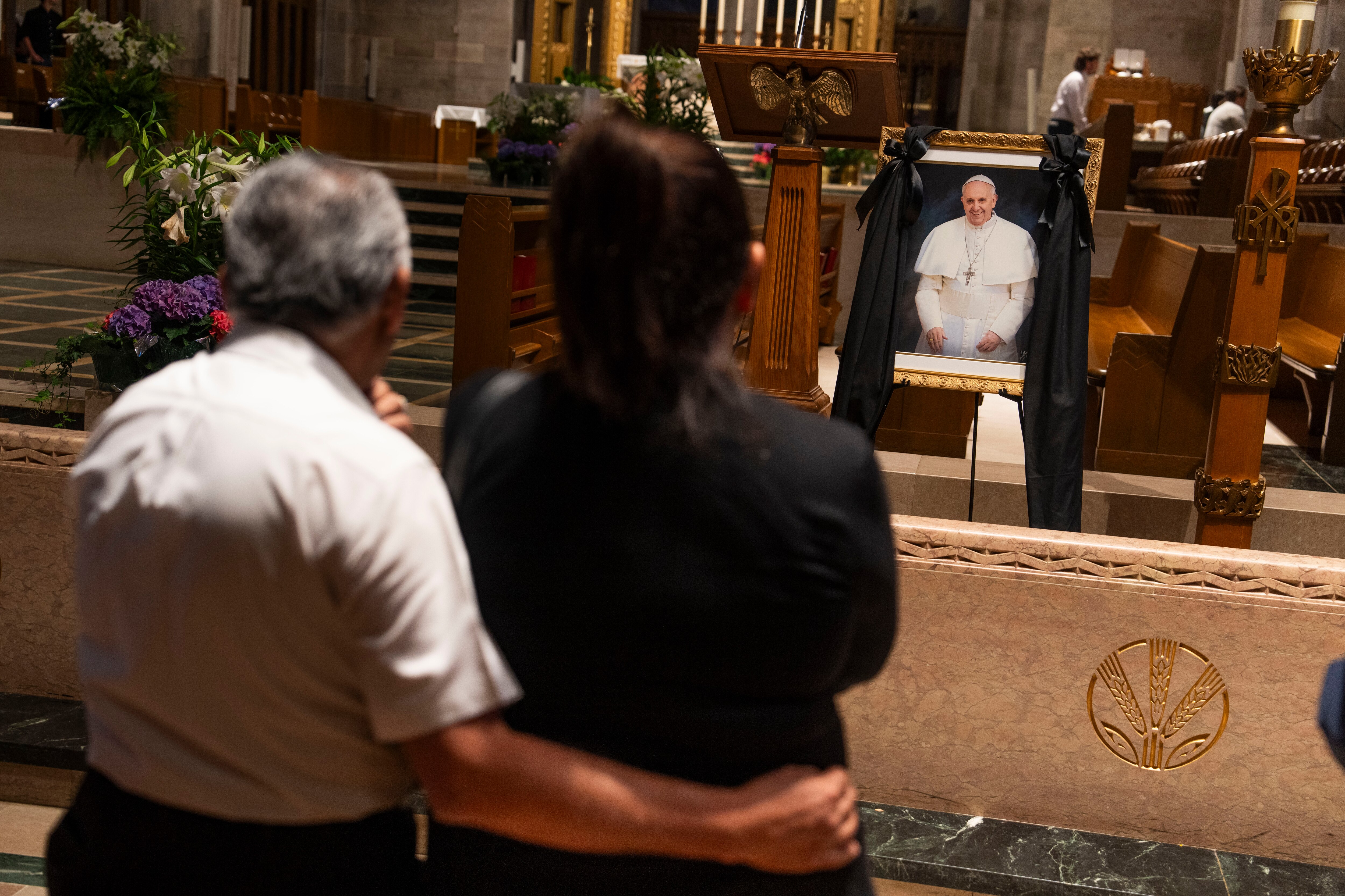 Leonor and Jose Rivera hold each other as they pay respects and mourn at a portrait of Pope Francis after a Mass at The Cathedral of Mary Our Queen in North Baltimore on Monday evening.