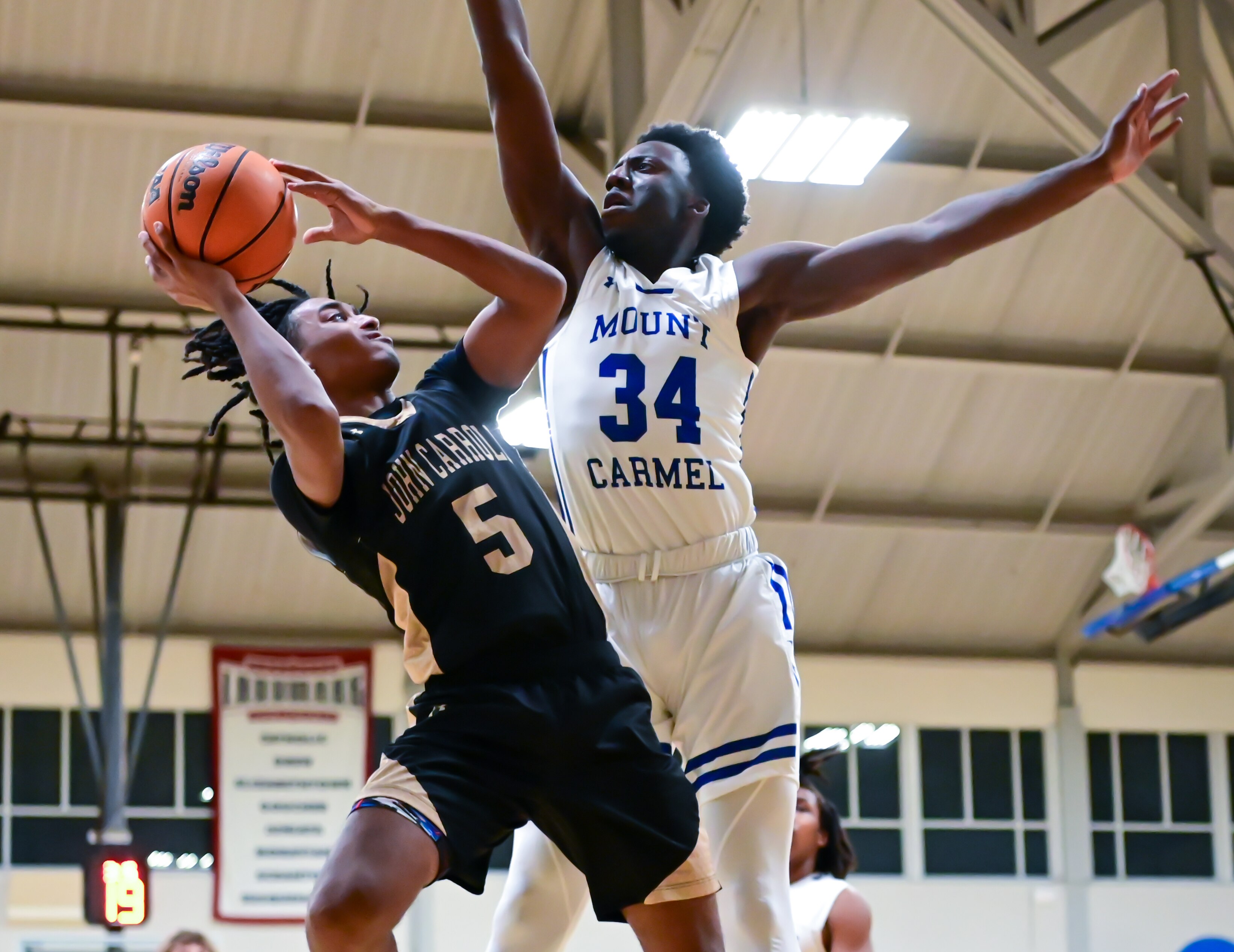 John Carroll's Caden Chinnia-Falline (5) tries to shoot against Mount Carmel's Allen Mordi during Friday night's Baltimore Catholic League Tournament quarterfinal match. The No. 6 Cougars advanced to the semifinals with a 79-63 victory over the Patriots at Goucher College.