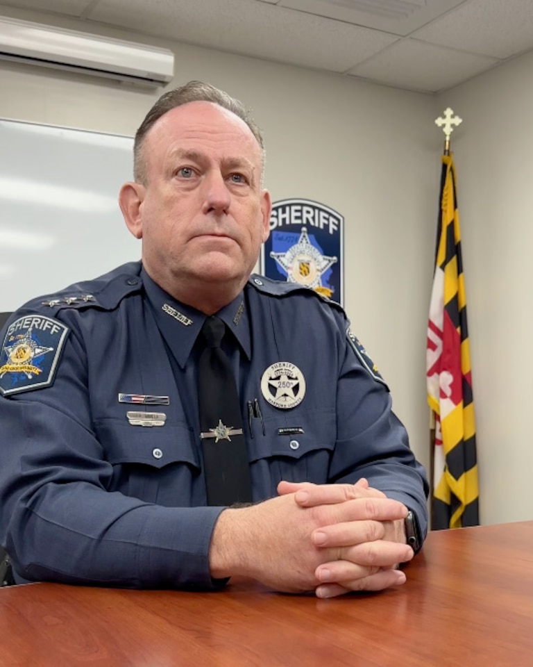 January 22, 2024 - Photograph of a man seated at the table with hands clasped, Maryland flag in the background. He wears the uniform of a sheriff.