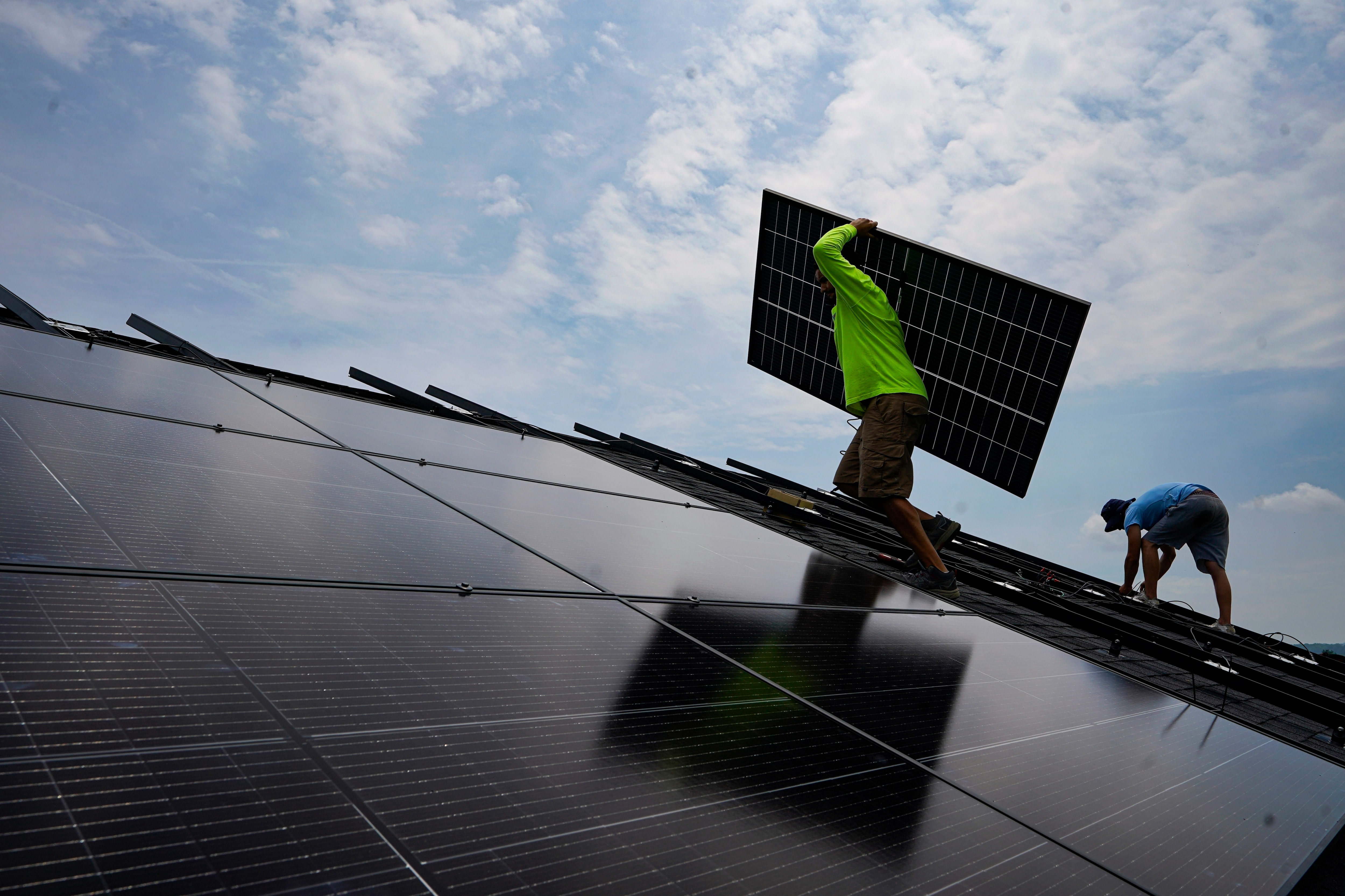 FILE - Nicholas Hartnett, owner of Pure Power Solar, carries a panel as he and Brian Hoeppner, right, install a solar array on the roof of a home in Frankfort, Ky., July 17, 2023.