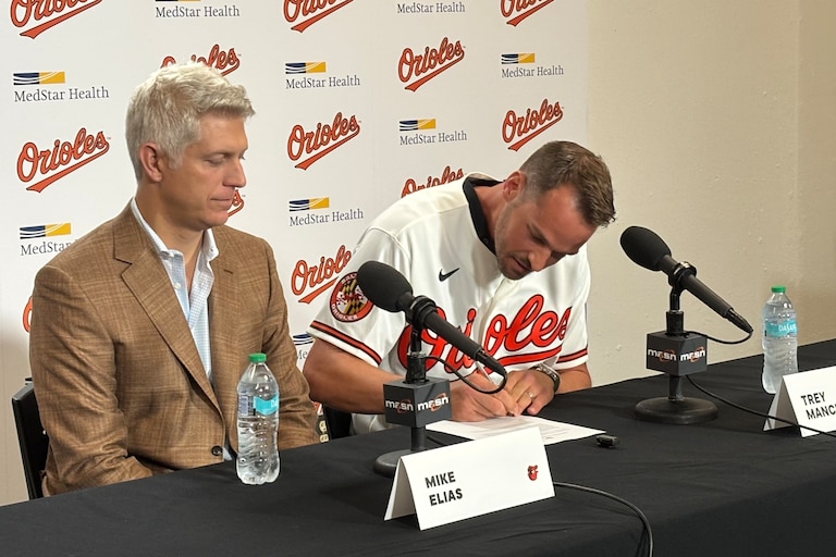 Trey Mancini signs a one-day contract with the Orioles as president of baseball operations Mike Elias looks on.