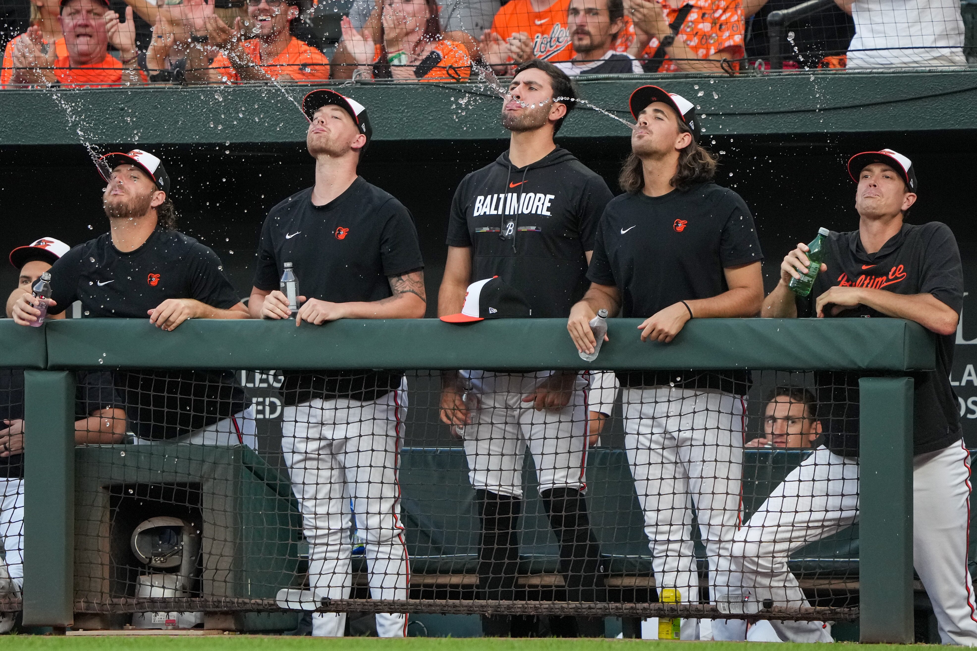 Baltimore Orioles starting pitchers spit out water from the dugout to celebrate catcher Adley Rutschman’s triple on Aug. 9, 2023.