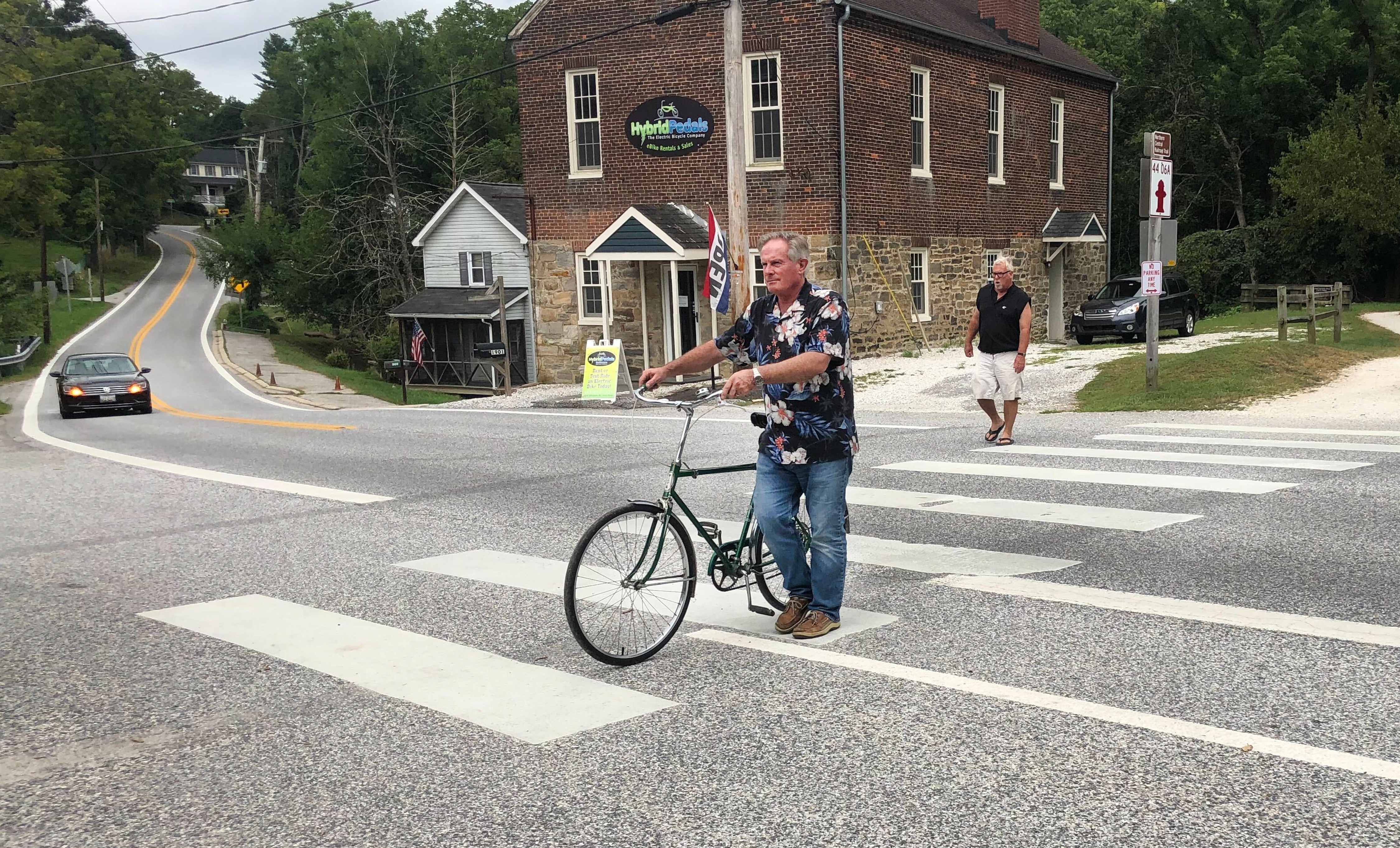 Buddy Sueck, who lives by the crossing, walks his bicycle across the intersection.