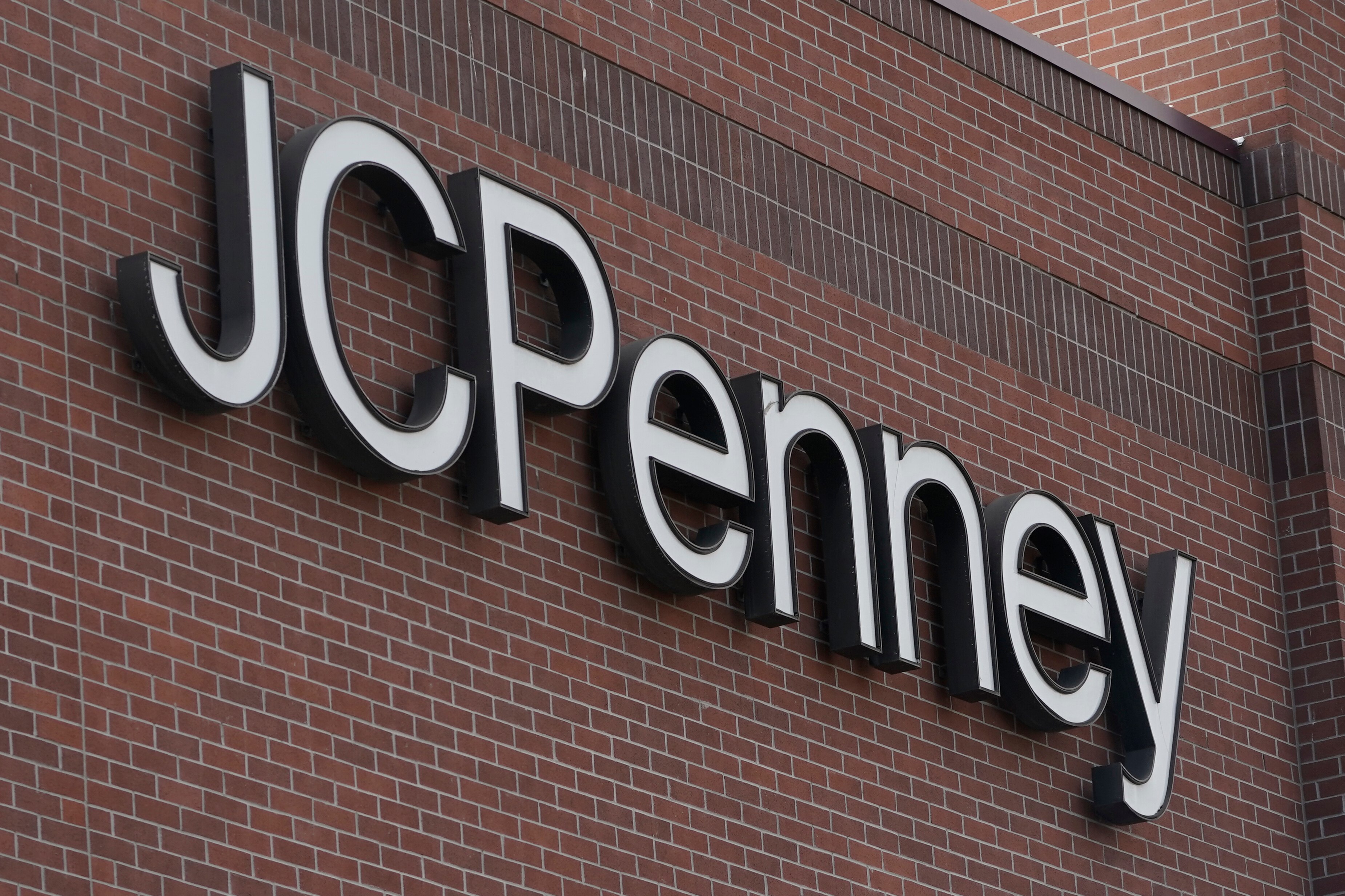 A JCPenney sign is displayed at one of the company's department store locations. The sign is plain white lettering against a brick wall.