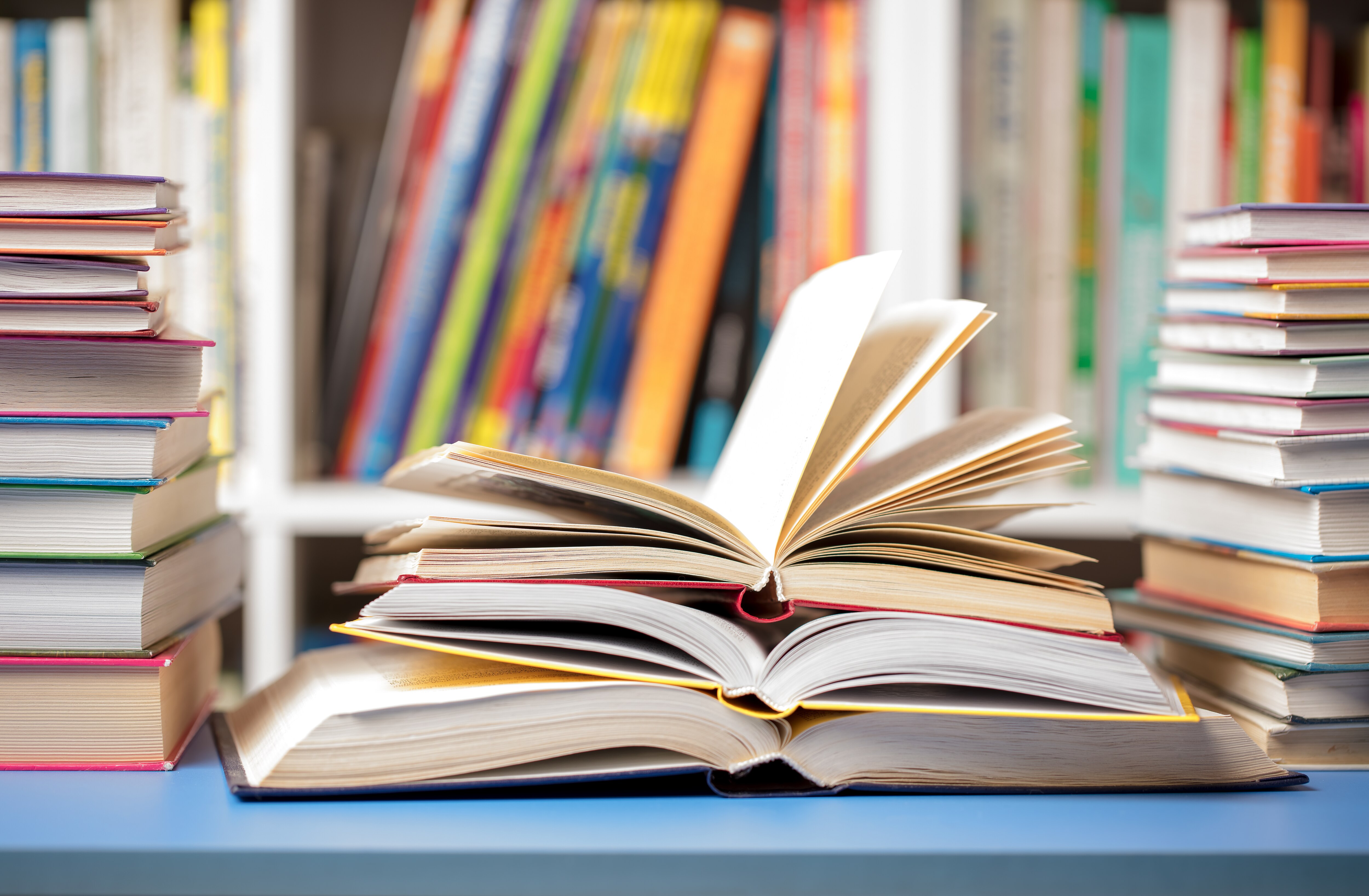 A DSLR photo of books at the library. Several books are arranged on a table with some open and others closed.