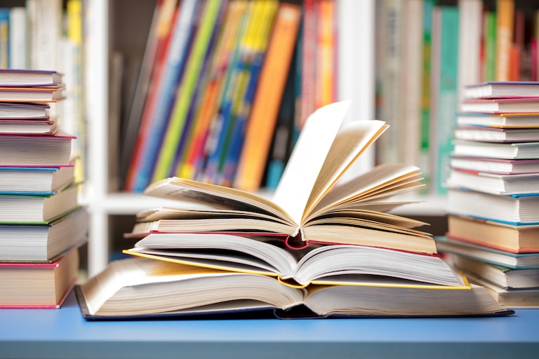 A DSLR photo of books at the library. Several books are arranged on a table with some open and others closed.