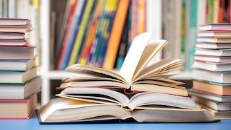 A DSLR photo of books at the library. Several books are arranged on a table with some open and others closed.