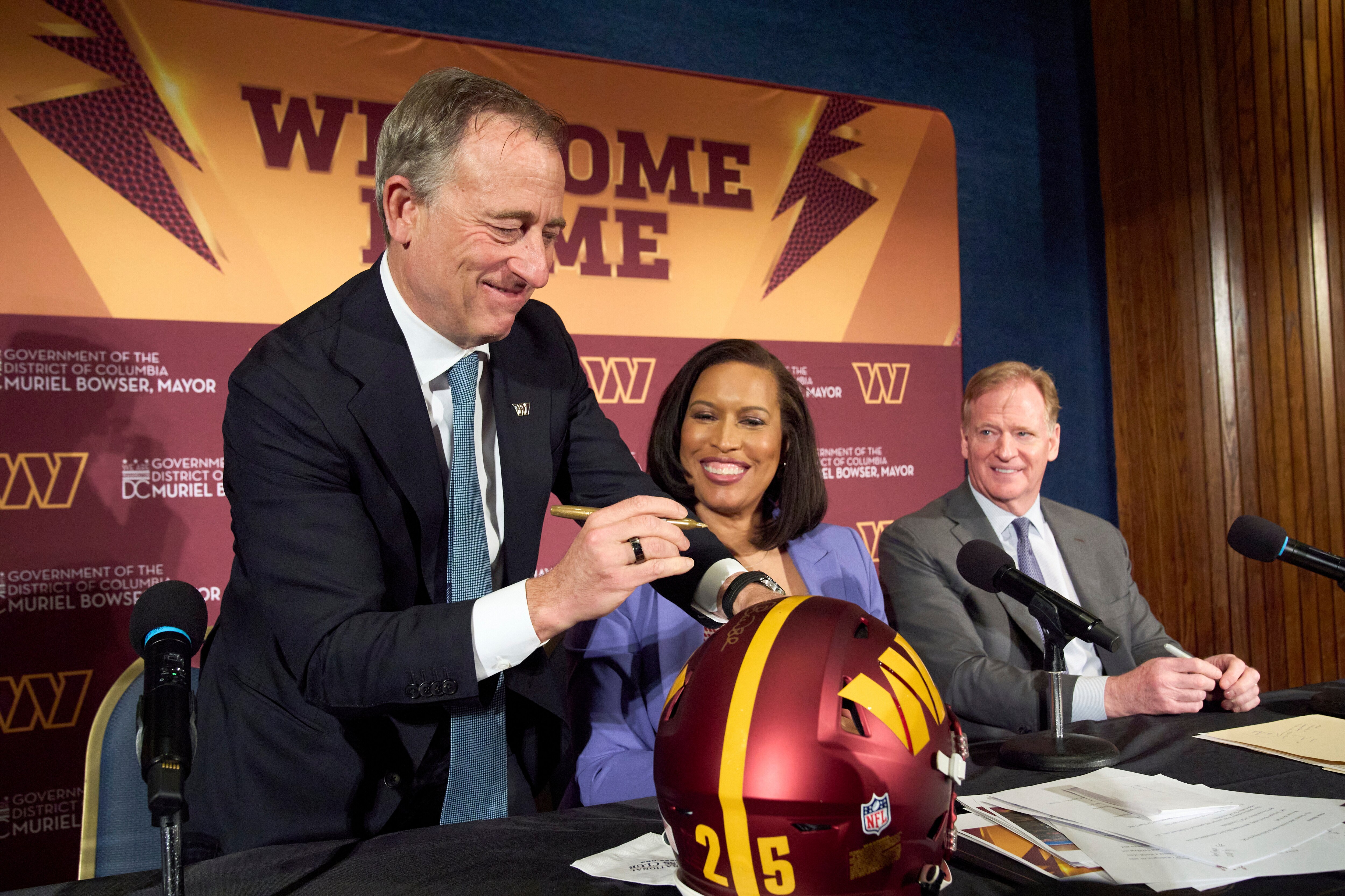 Washington Commanders controlling owner Josh Harris, from left, signs a helmet along with District of Columbia Mayor Muriel Bowser and NFL Commissioner Roger Goodell after an announcement about a new home for the NFL football team on the site of the old RFK Stadium, Monday, April 28, 2025, at the National Press Club in Washington.
