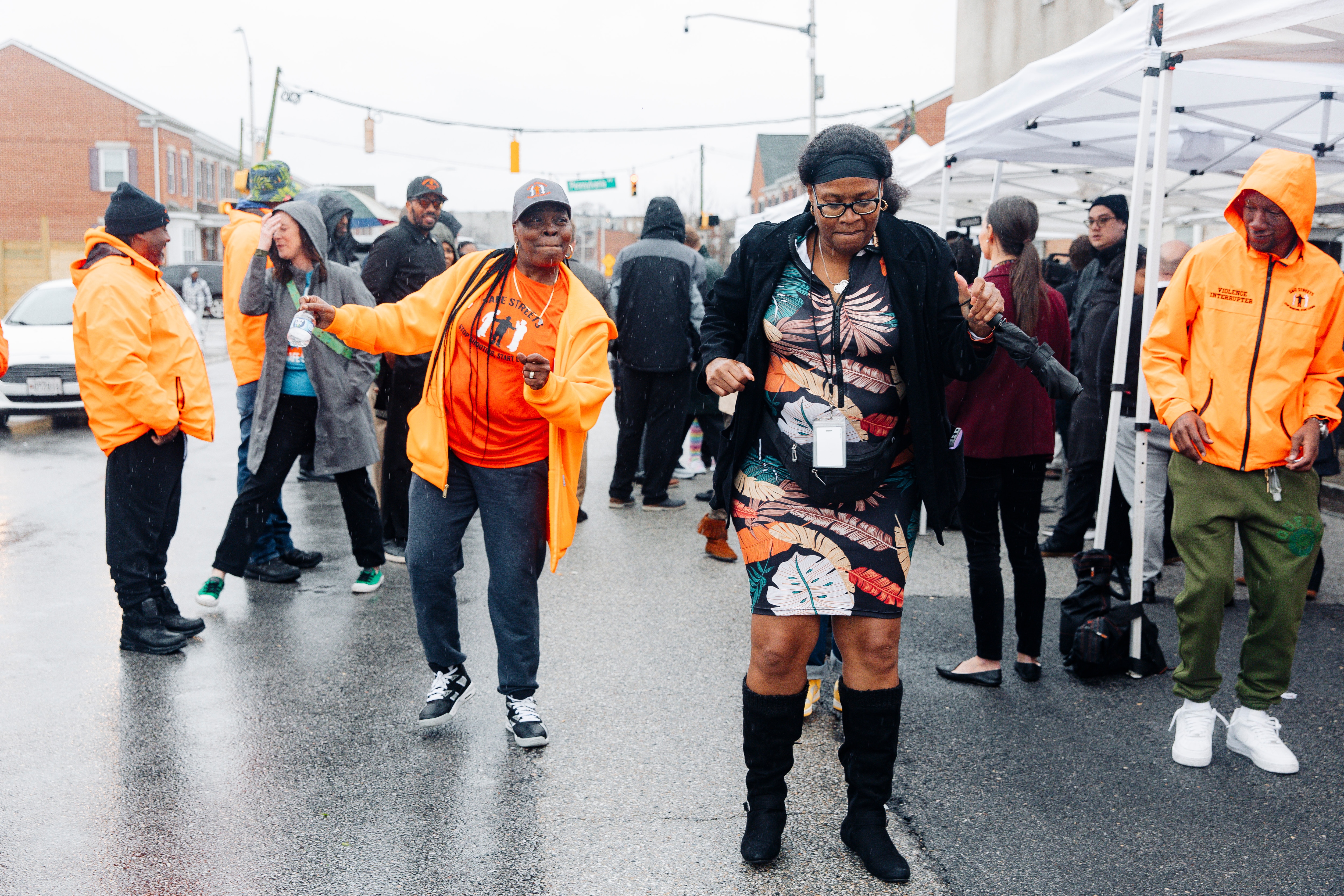 Catholic Charities Peer Recovery Specialist Genese Hubbard, right, and Safe Streets Site Director Nicole Warren dance in the rain after the event commemorating a year without homicides, in front of the Safe Streets Penn North site managed by Catholic Charities, on Wednesday, March 6, 2024 in Baltimore, MD. (Wesley Lapointe / for The Baltimore Banner) 