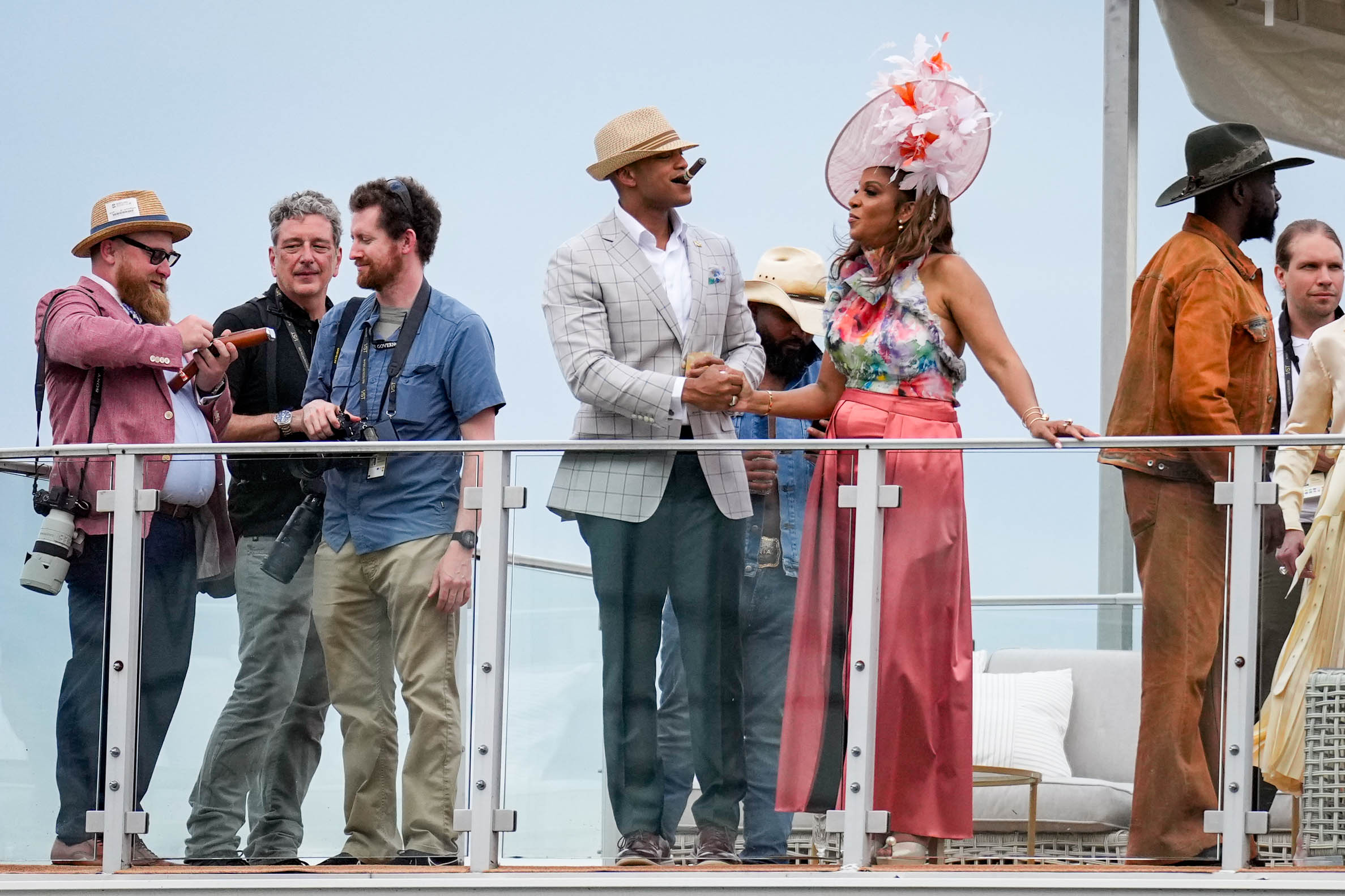 Gov. Wes Moore, center, smokes a cigar and holds hands with his wife, First Lady Dawn Flythe Moore ahead of the 150th running of the Preakness Stakes at Pimlico Race Course in Baltimore, Md. on Saturday, May 17, 2025.