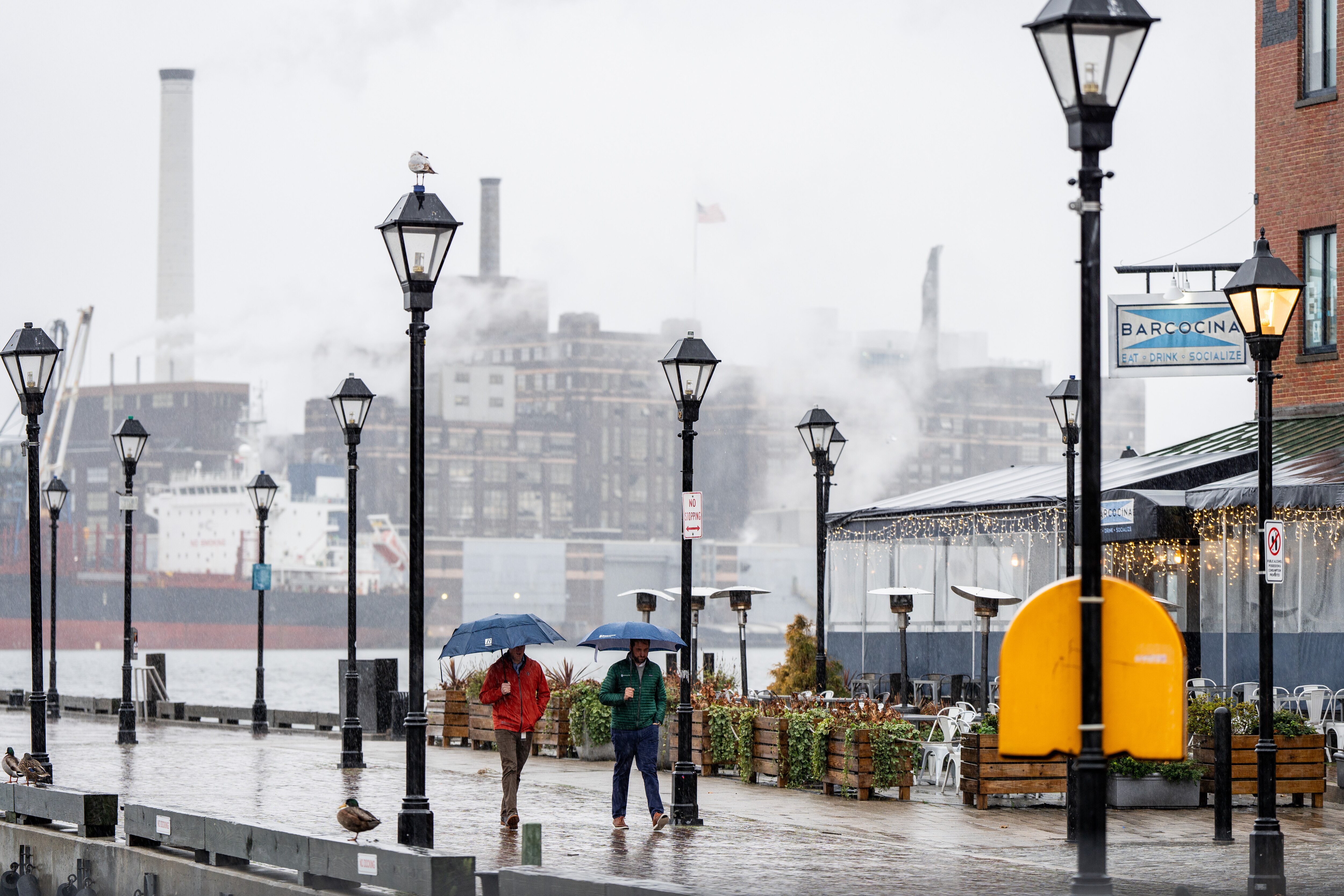 Two people walk through Fells Point on a rainy Tuesday, Jan. 9, 2024, with the Domino Sugars plant in the background.