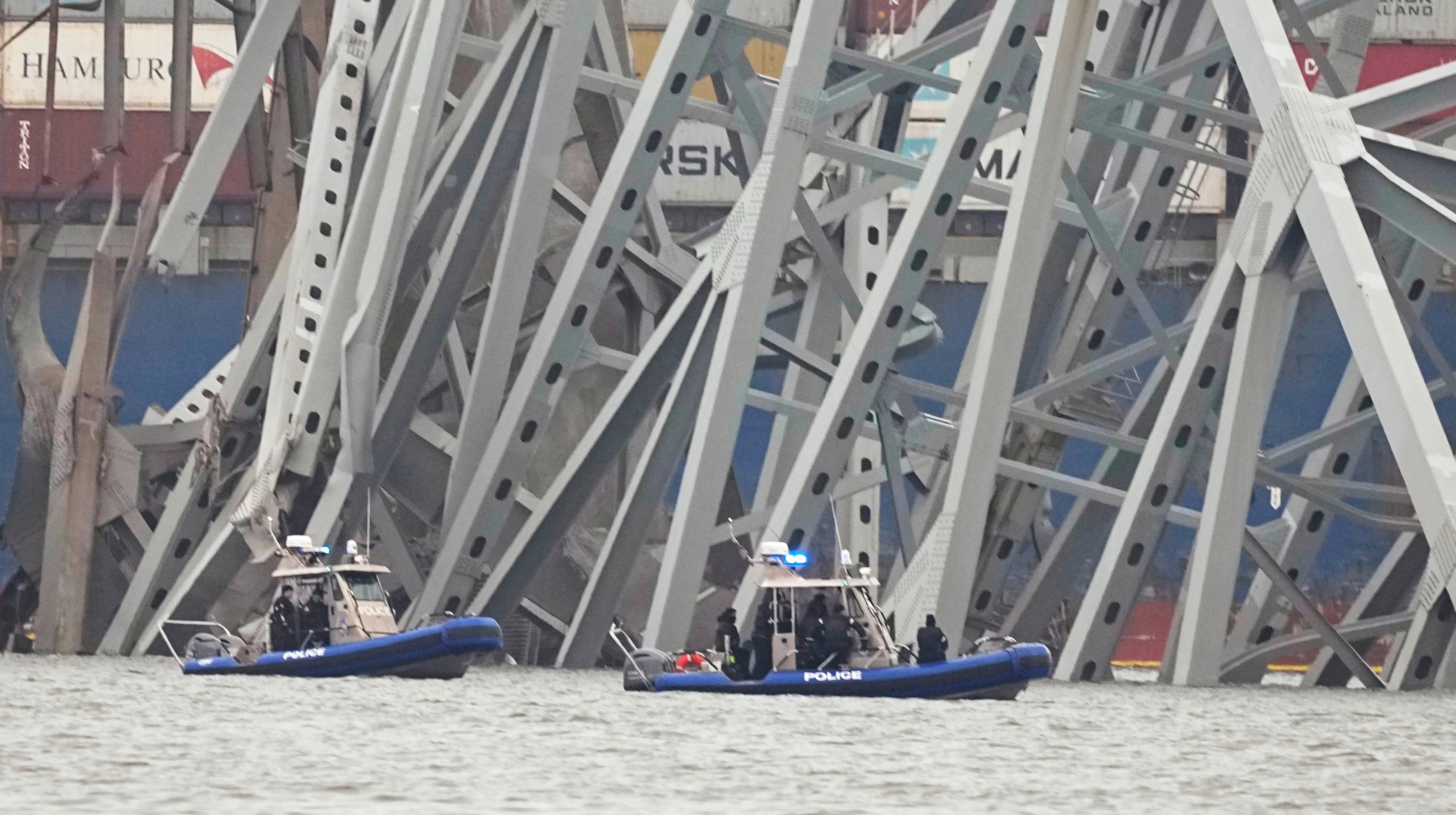 Police boats work around a cargo ship that is stuck under part of the structure of the Francis Scott Key Bridge after the ship hit the bridge.