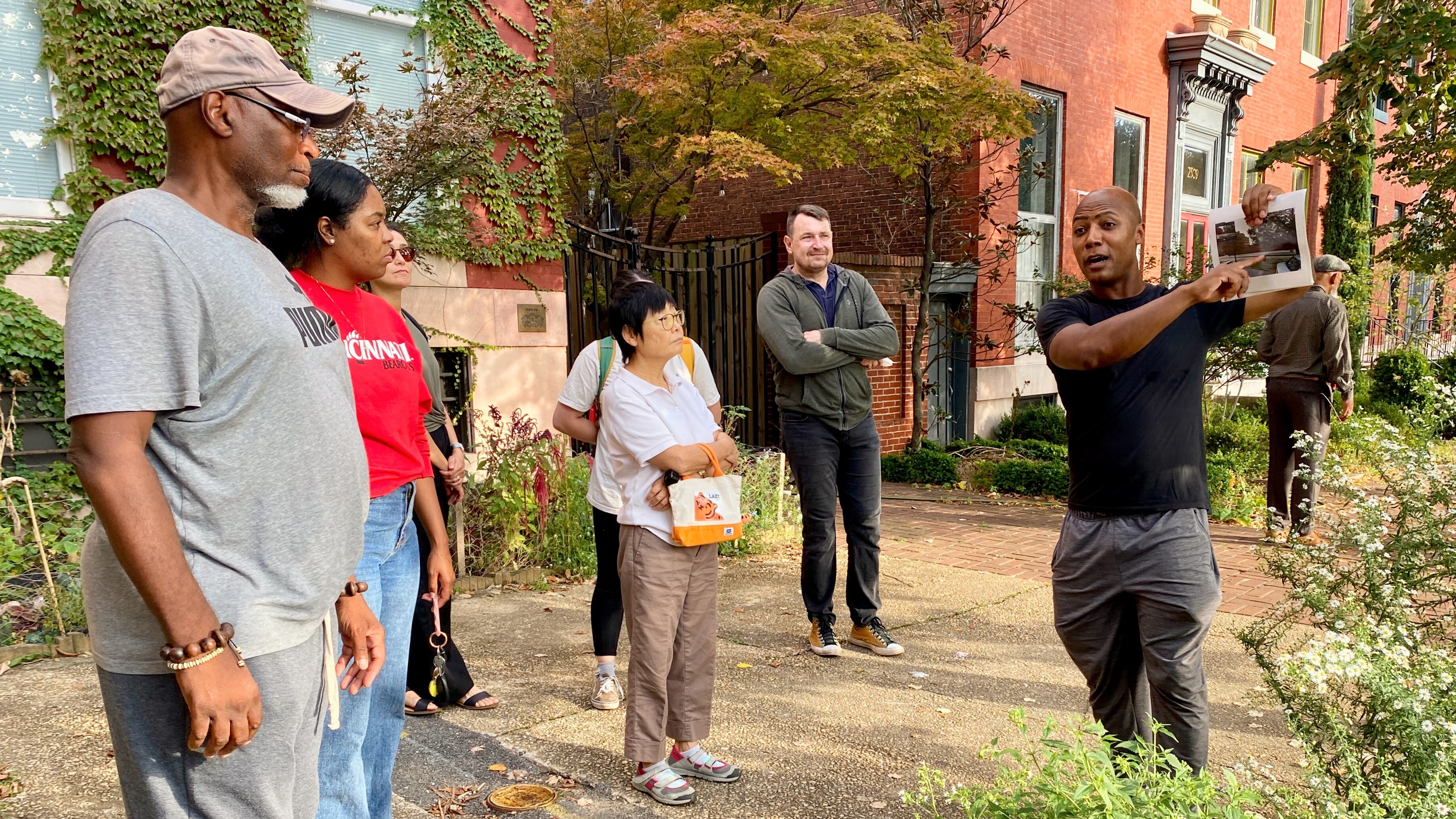 Kelly Cross, community activist and resident of  Old Goucher neighborhood in Central Baltimore, holds a picture for the group of visitors showcasing how the neighborhood looked before they successfully led the community-led effort to plant more trees.