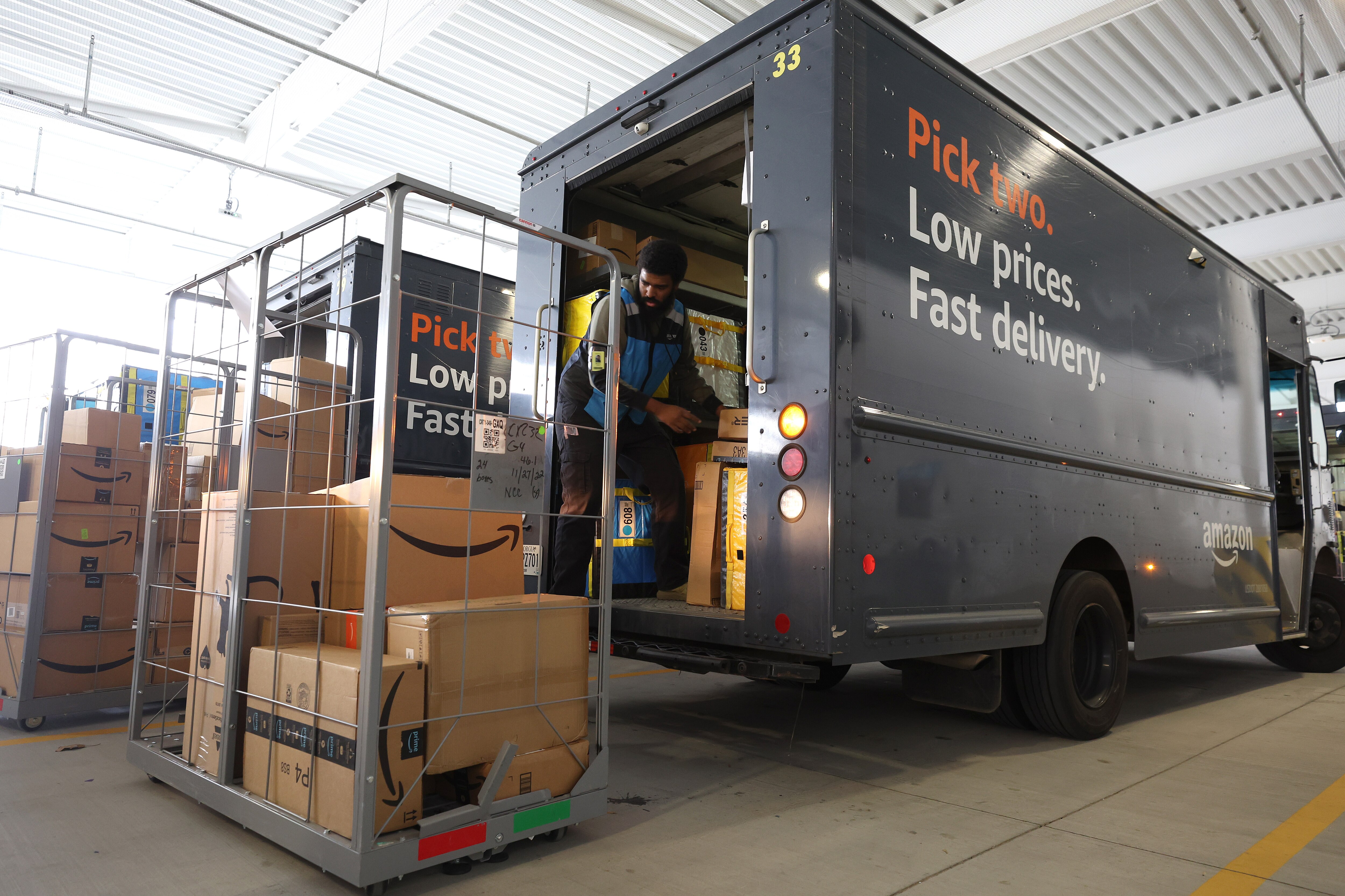 A man loads packages from a metal pallet into the back of an Amazon box truck.