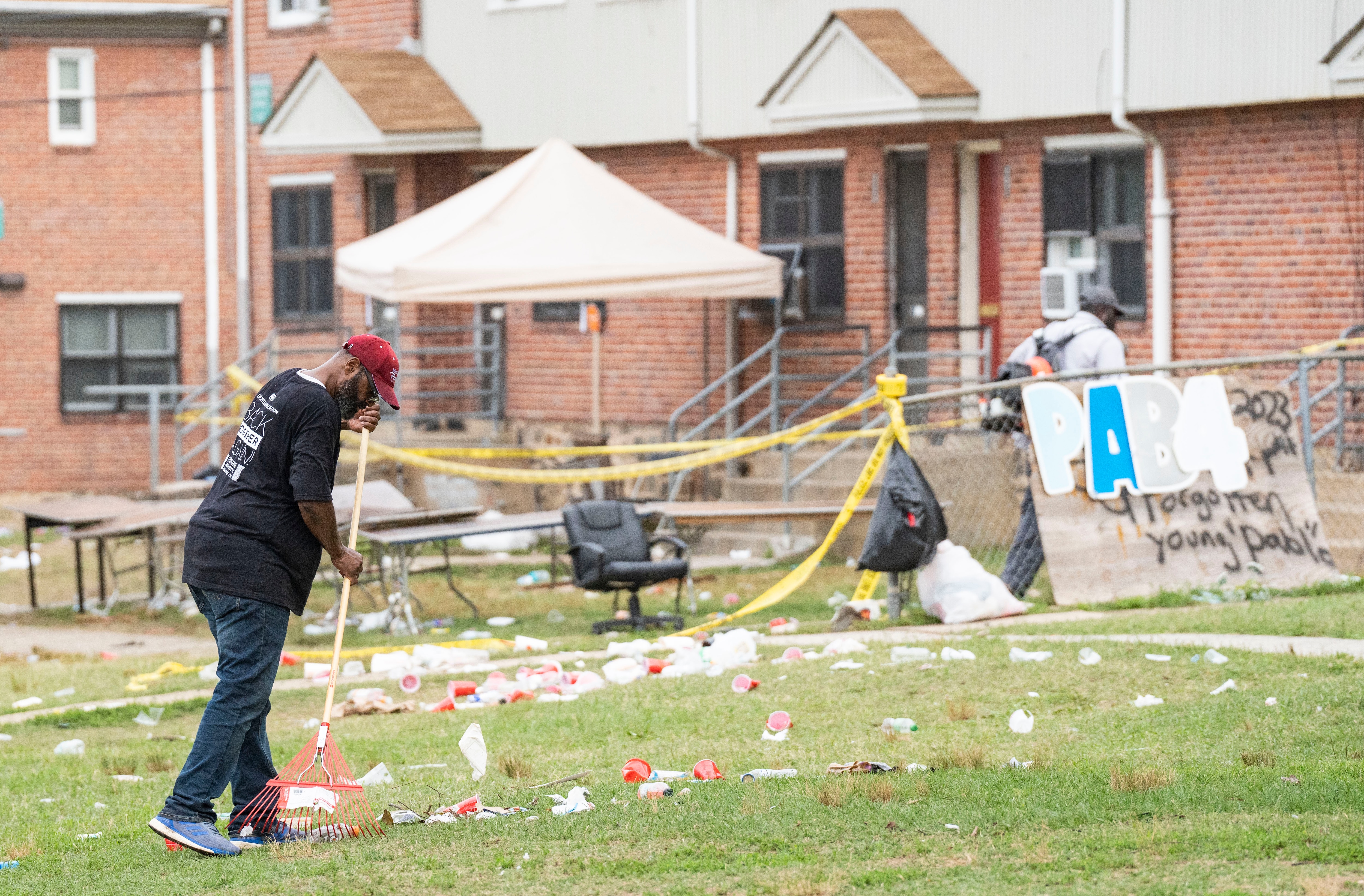 A cleaning crew member rakes garbage at the crime scene on Elarton Court in Brooklyn following a shooting on Sunday, July 2, 2023.