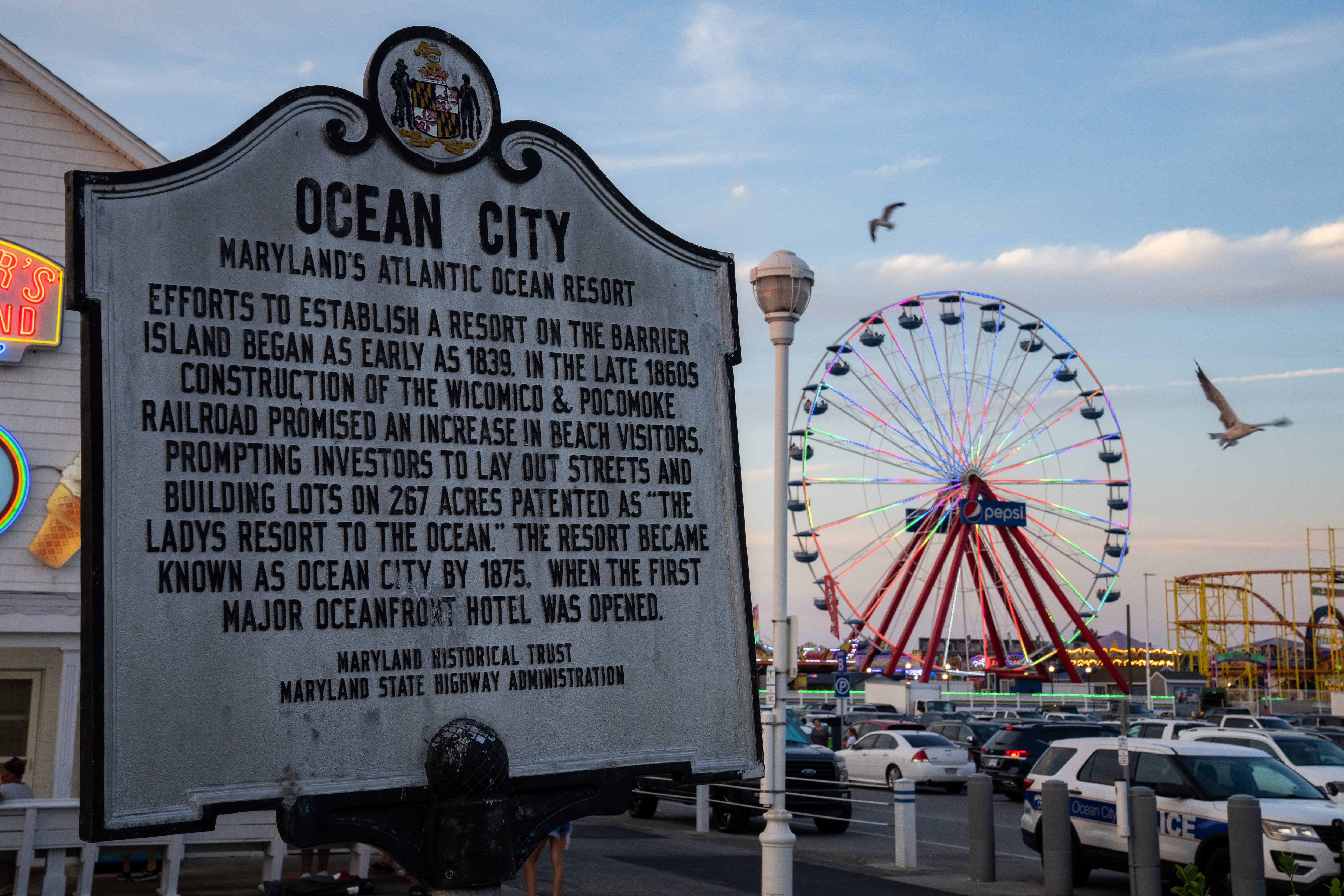 A sign detailing Ocean City’s history, with the ferris wheel lit rainbow in the righthand background.