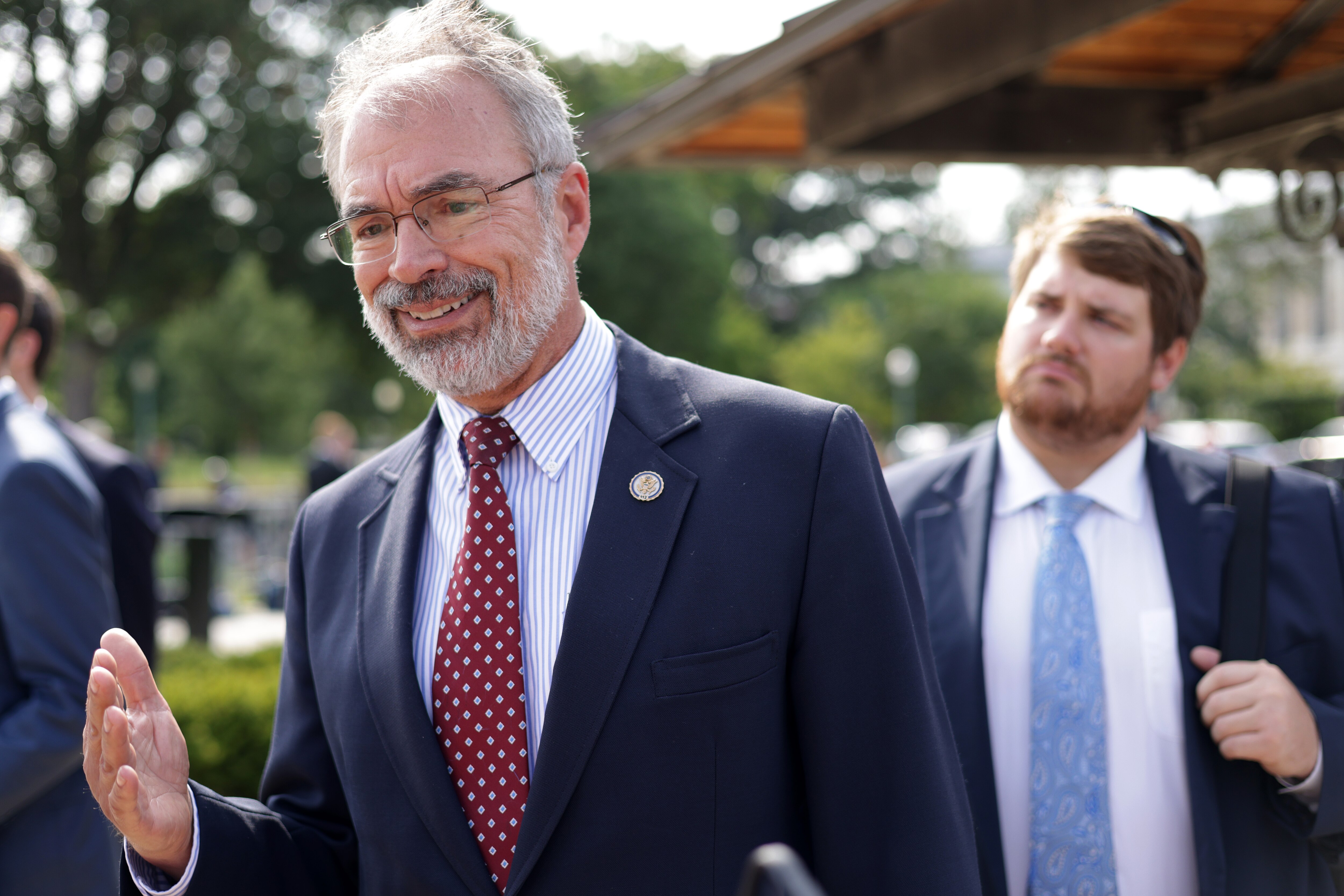 A man with a gray beard and glasses and wearing a dark suit with the red tie and Congressional member pin.