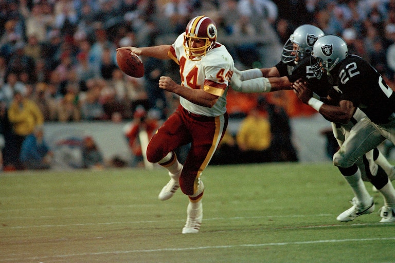 Washington Redskins running back John Riggins is pursued by Los Angeles Raiders defenders as he carries the ball during the Super Bowl XVIII in 1984.