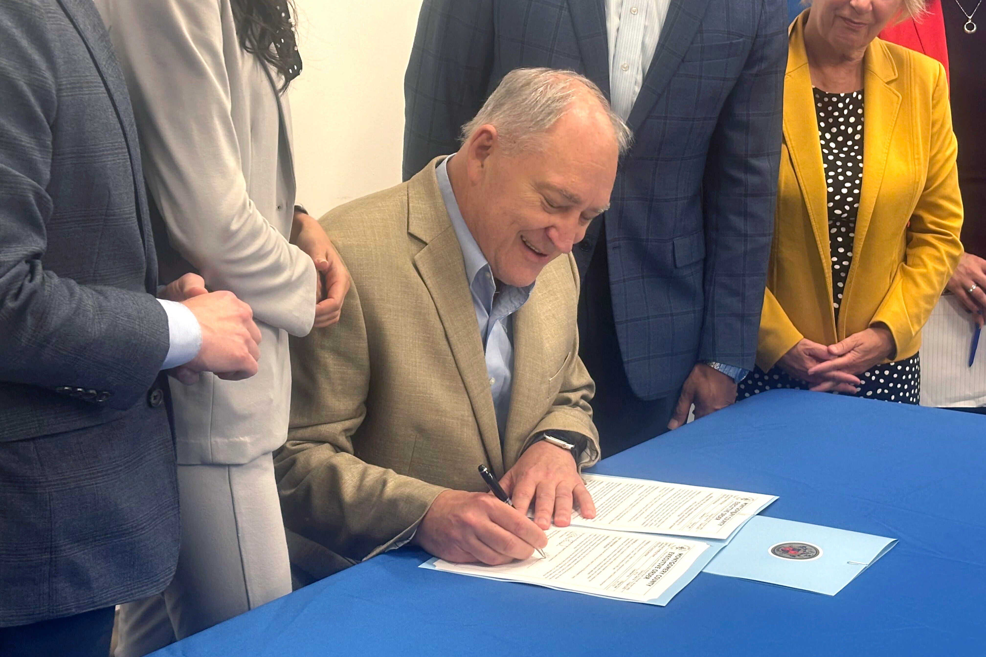 Montgomery County Executive Marc Elrich signs an executive order Friday issuing a six-month moratorium on data center permits, while flanked by supporters. The temporary ban is Elrich’s answer to months of debate on the issue.