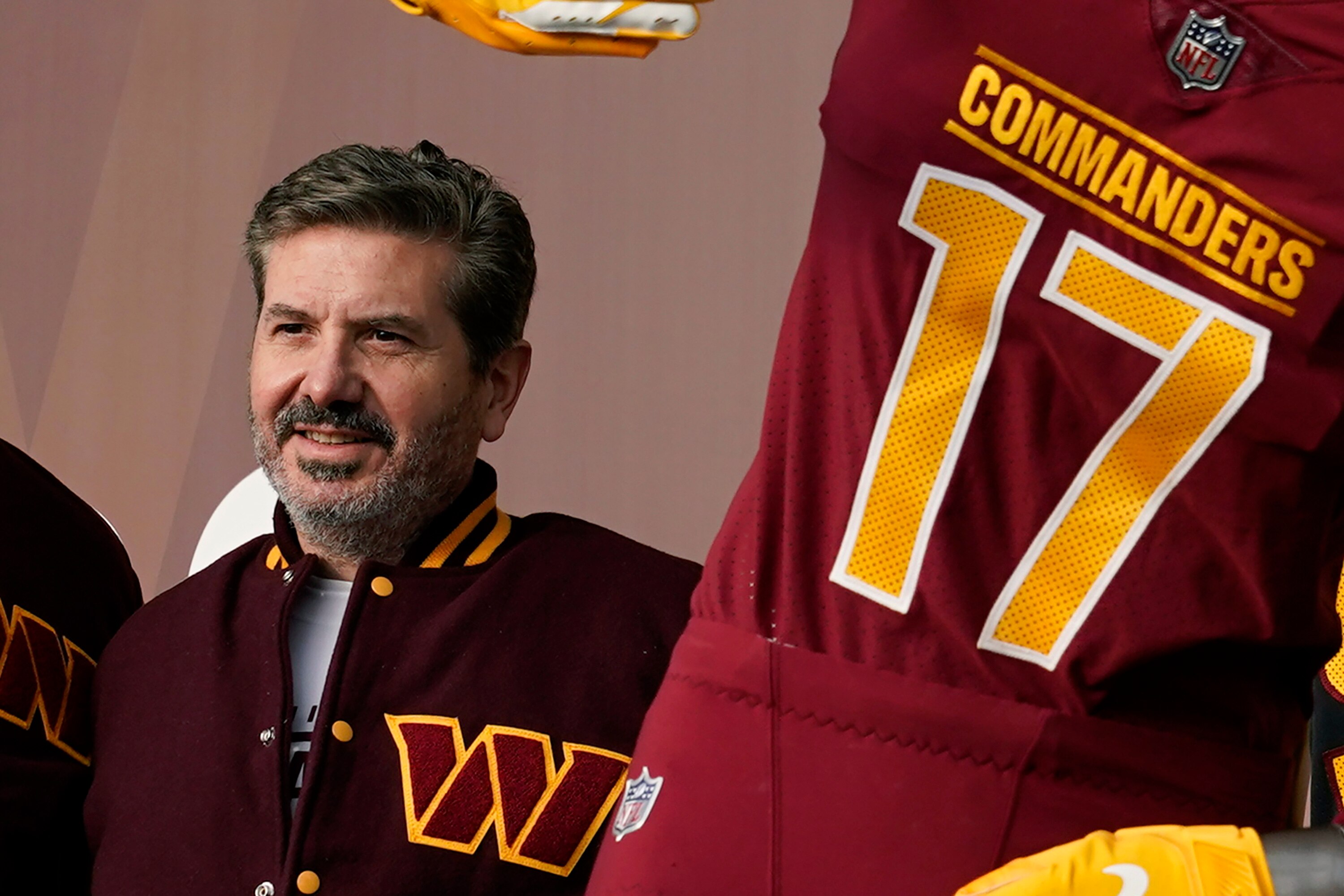 This photo shows Washington Commanders owner Dan Snyder standing near a jersey for the team.