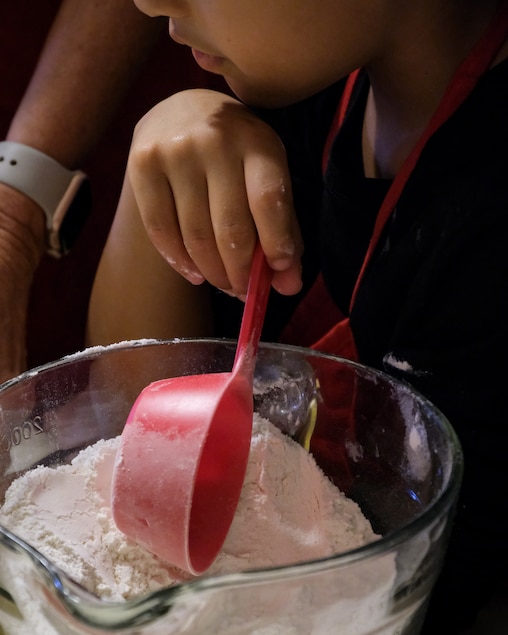 Micah Walker stands ready to add flour as her grandmother, Beth Rannie, mixes the batter for pizelles.
