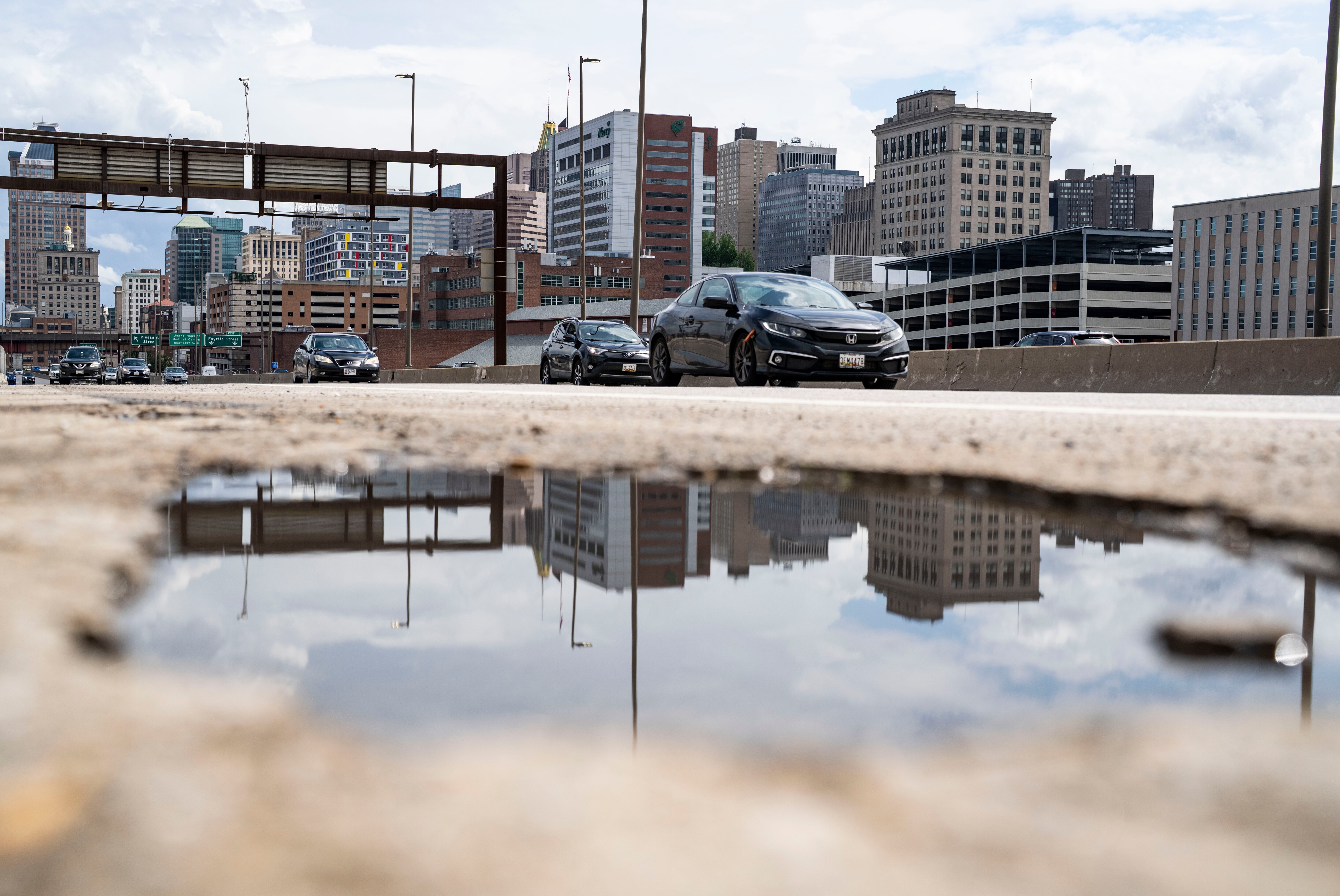 Baltimore City buildings reflect in water inside of a pothole on I-83 in Baltimore, Thursday, May 22, 2025.