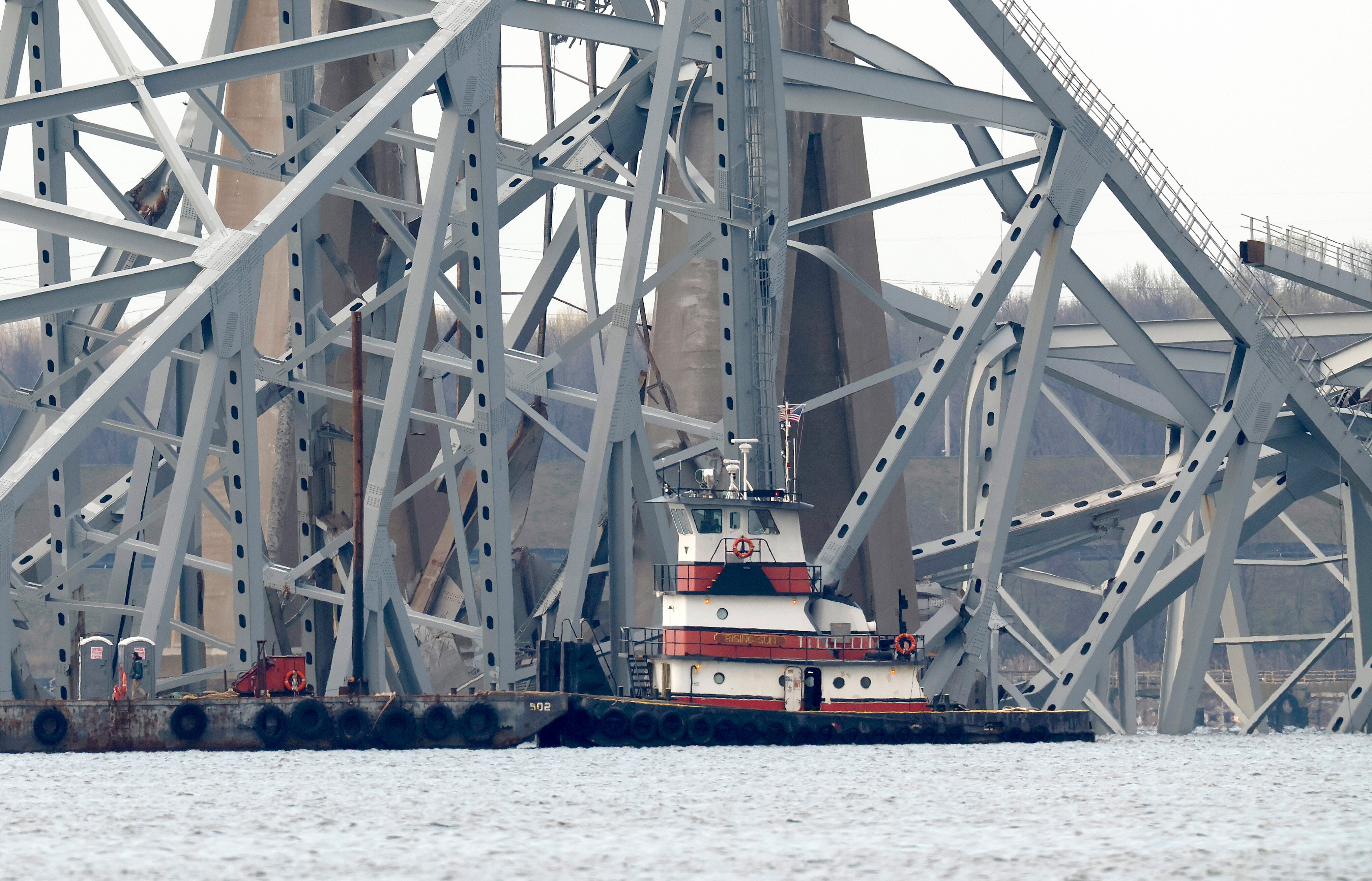 A tugboat and barge, shown here March 29, move past the twisted remains of the Francis Scott Key Bridge, which was destroyed when a cargo ship collided with it in the early hours of March 26. The bridge collapsed after being struck by the massive cargo ship Dali.