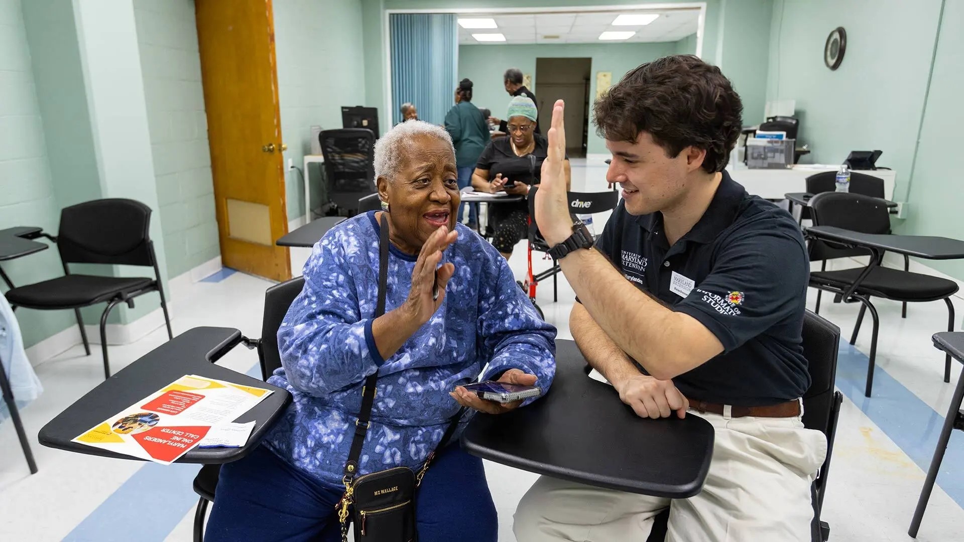 Francena Bean-Waters of Baltimore and UMD Tech Extension Educator Blaise Brennan '18 share a high-five after working through a smartphone operation question together.