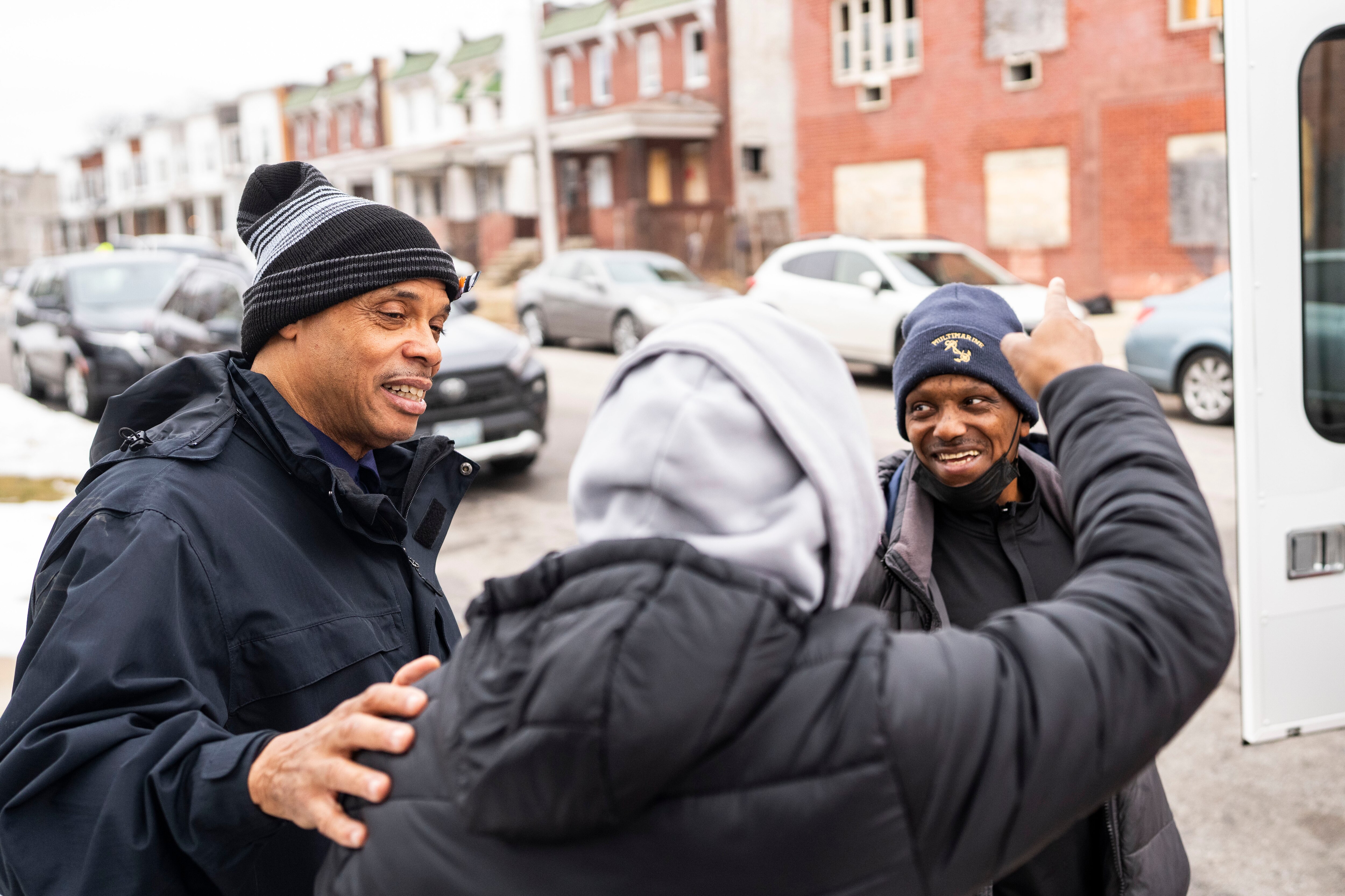 Peter Griffin, left, director of outreach and intake for Helping Up Mission, and Keith Dunkley, right, greet Ruben Gregg during a stop with the nonprofit’s Mobile Street Outreach team in Baltimore last month.