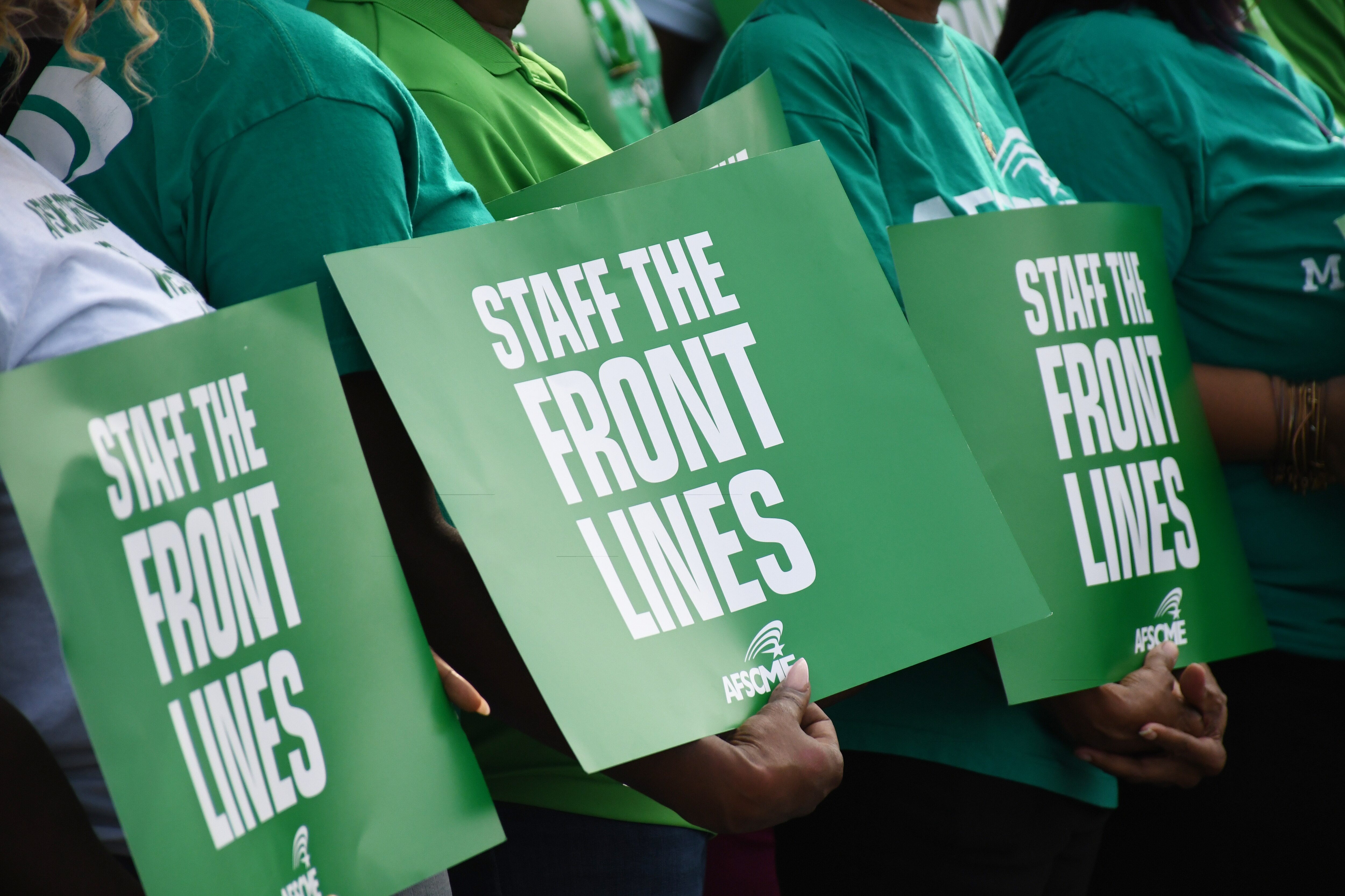 Members of the AFSCME union hold up signs reading "staff the front lines" during an event with Gov. Wes Moore, Baltimore Mayor Brandon Scott and national union President Lee Saunders outside the union building in southwest Baltimore on Saturday, Sept. 9, 2023.