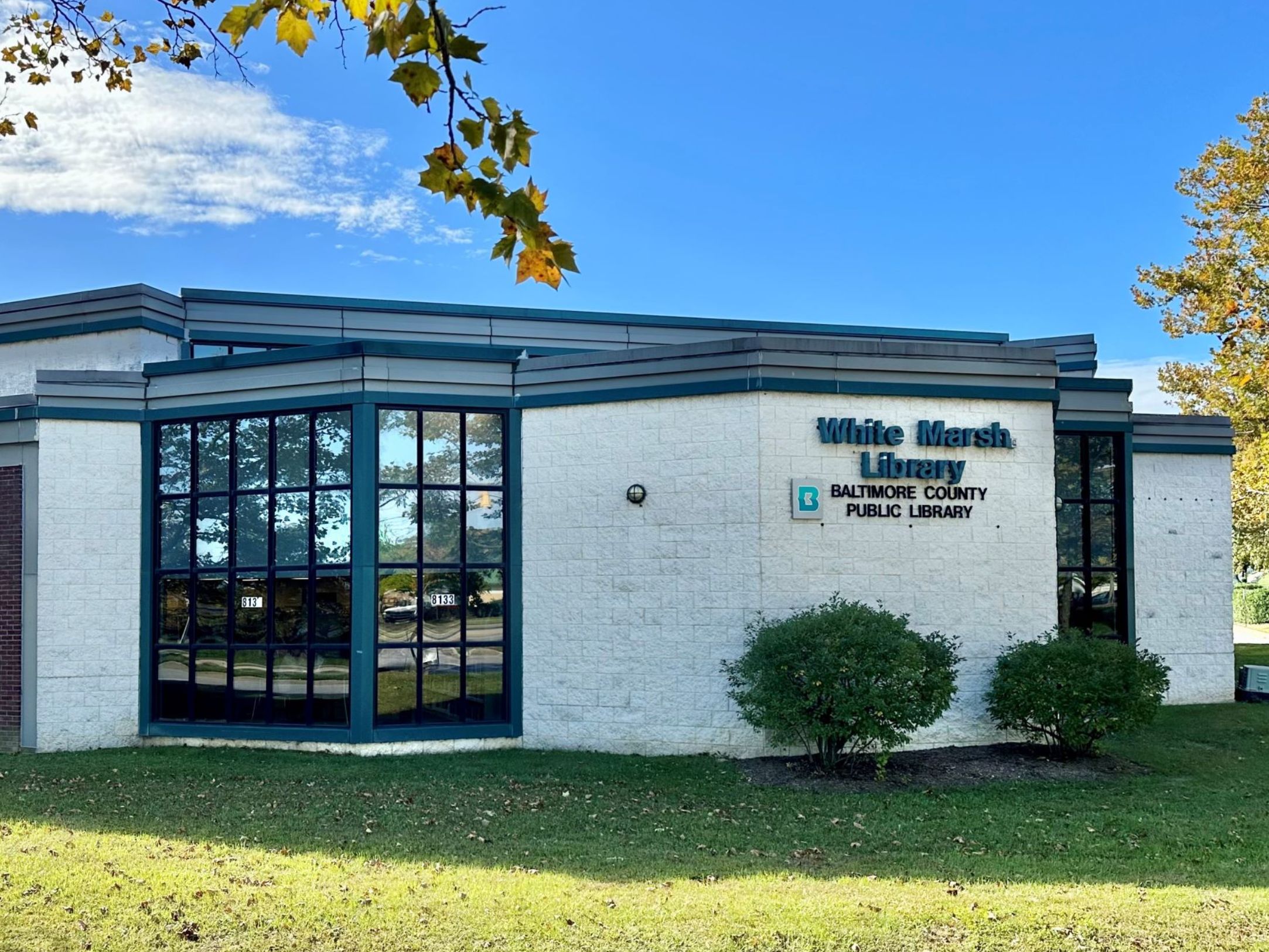 An exterior view of the White Marsh branch of the Baltimore County Public Library. The white building is relatively short, with large glass windows.