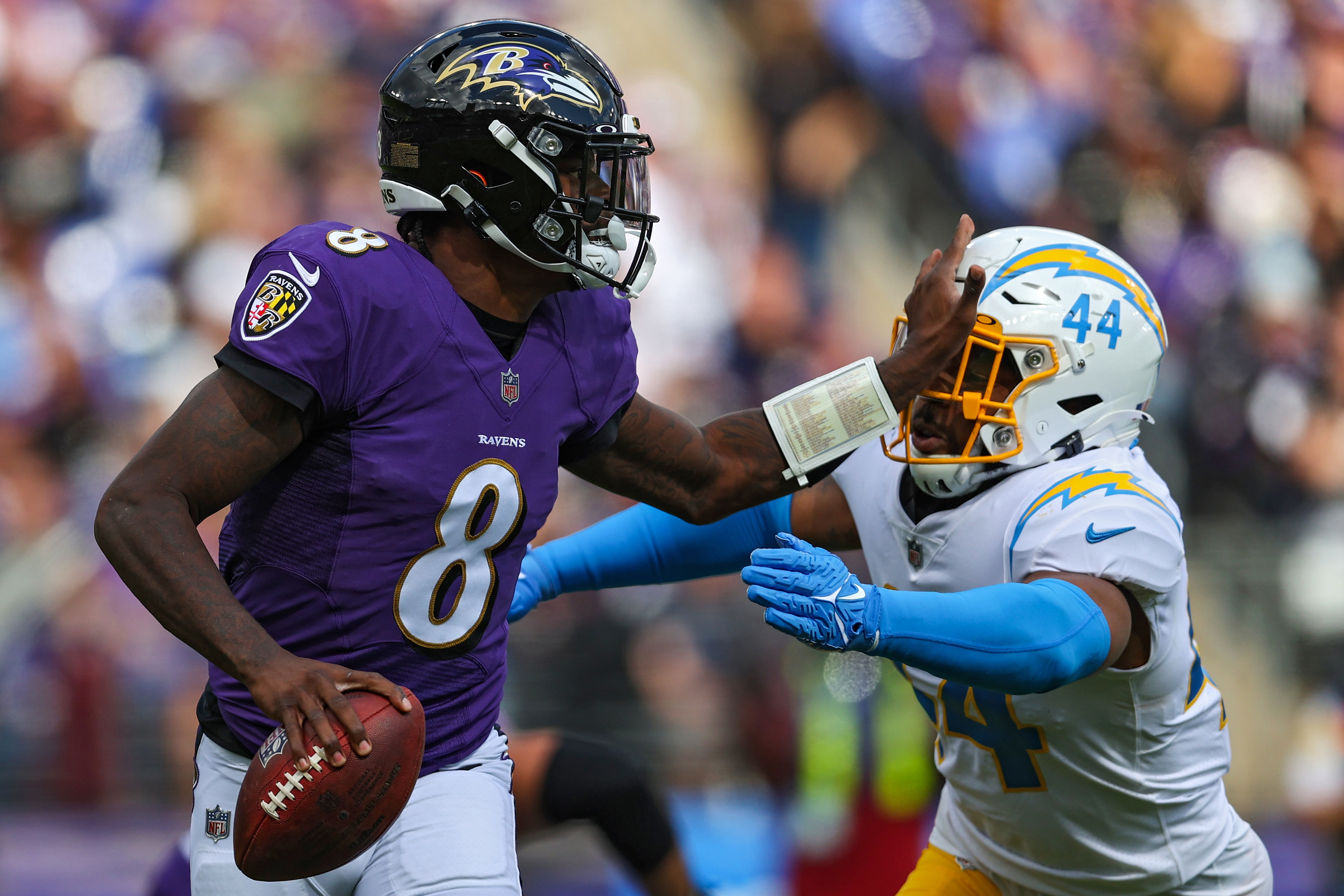 Quarterback Lamar Jackson #8 of the Baltimore Ravens stiff arms outside linebacker Kyzir White #44 of the Los Angeles Chargers during the first half at M&T Bank Stadium on October 17, 2021 in Baltimore, Maryland.