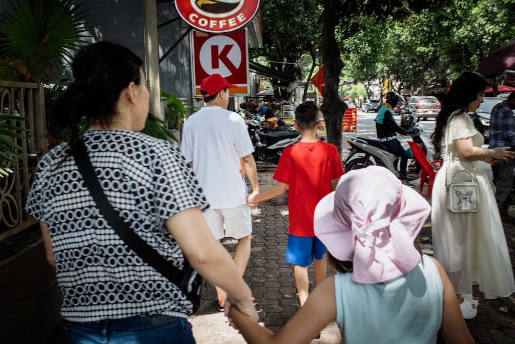 Dong Nai, Vietnam - Aug 2, 2026: Danny Hoang, 56, holds his son’s hand and Melissa Tran, 44, holds her daughter’s hand, while walking around the streets of Dong Nai, Vietnam on August 2, 2026. Rosem Morton for The Baltimore Banner