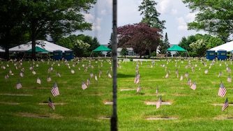 Flags placed by members of the Young Marines and Girl Scouts marking the gravesites of veterans are reflected in a statue at Dulaney Valley Memorial Gardens in Timonium on May 25, 2024.