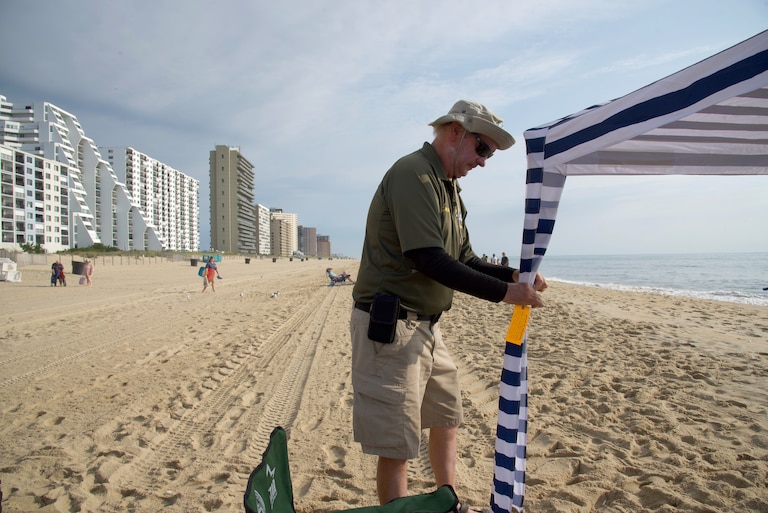 Tim Miller attaches an orange tag to an unattended canopy outside Condo Row in Ocean City on Aug. 16.