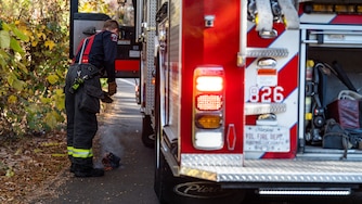 Prince George’s County firefighter Jacob Smith puts a smoldering piece of wood on the side of the truck during a woods fire call in District Heights, Md. on Tuesday, Nov. 14, 2023.