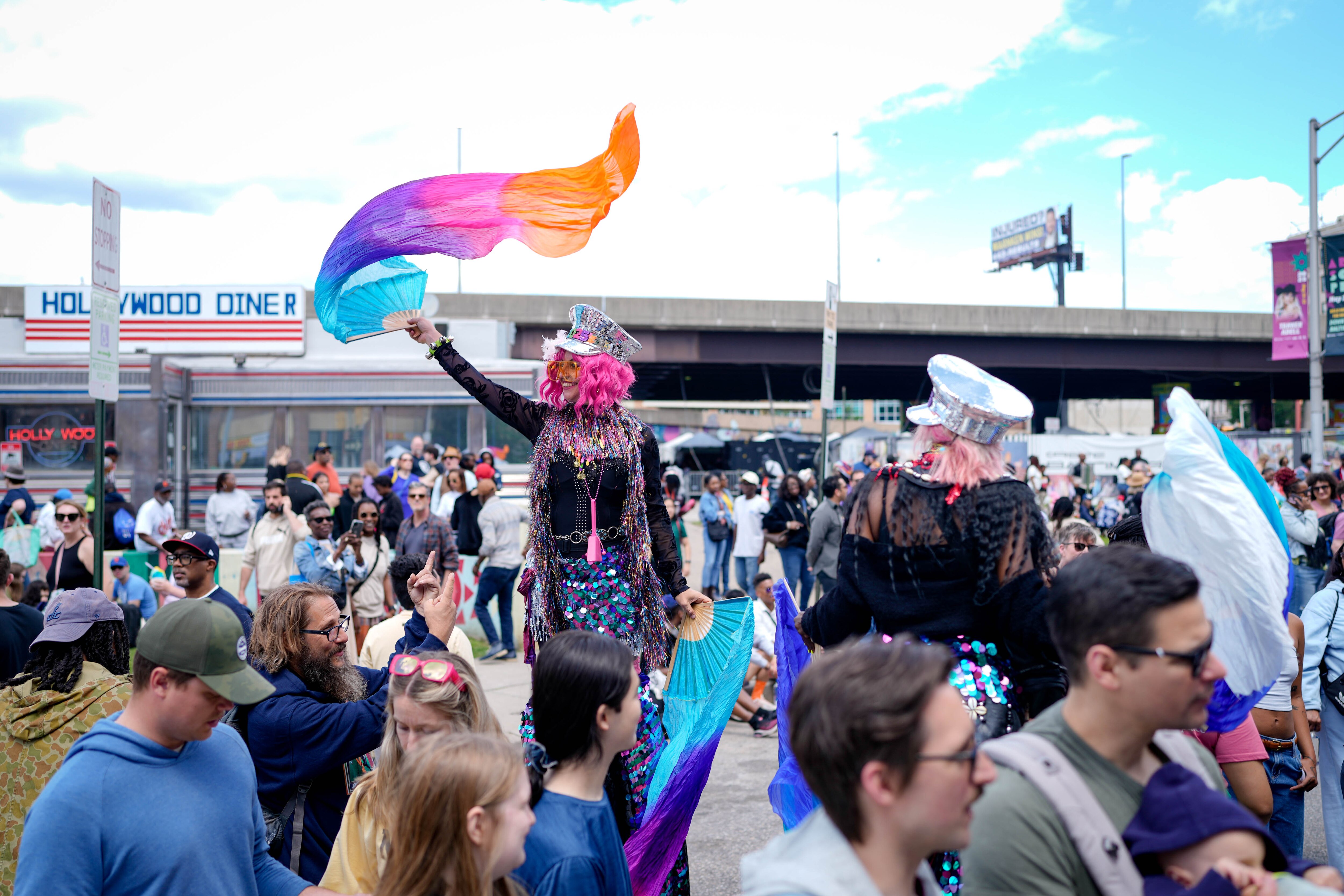 “Shorty,” left, a stilts performer with Baltimore Hoop Love, walks through the crowd waving a colorful scarf as festival attendees wait in line for food at Artscape in downtown Baltimore, Md. on Saturday, May 24, 2025.