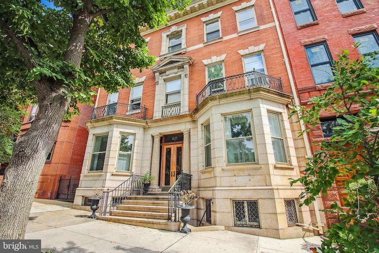 A street-level view of a classically beautiful residential building. A red brick building with white marble on the first floor, black iron railings and a large wooden front door stained in warm tone.
